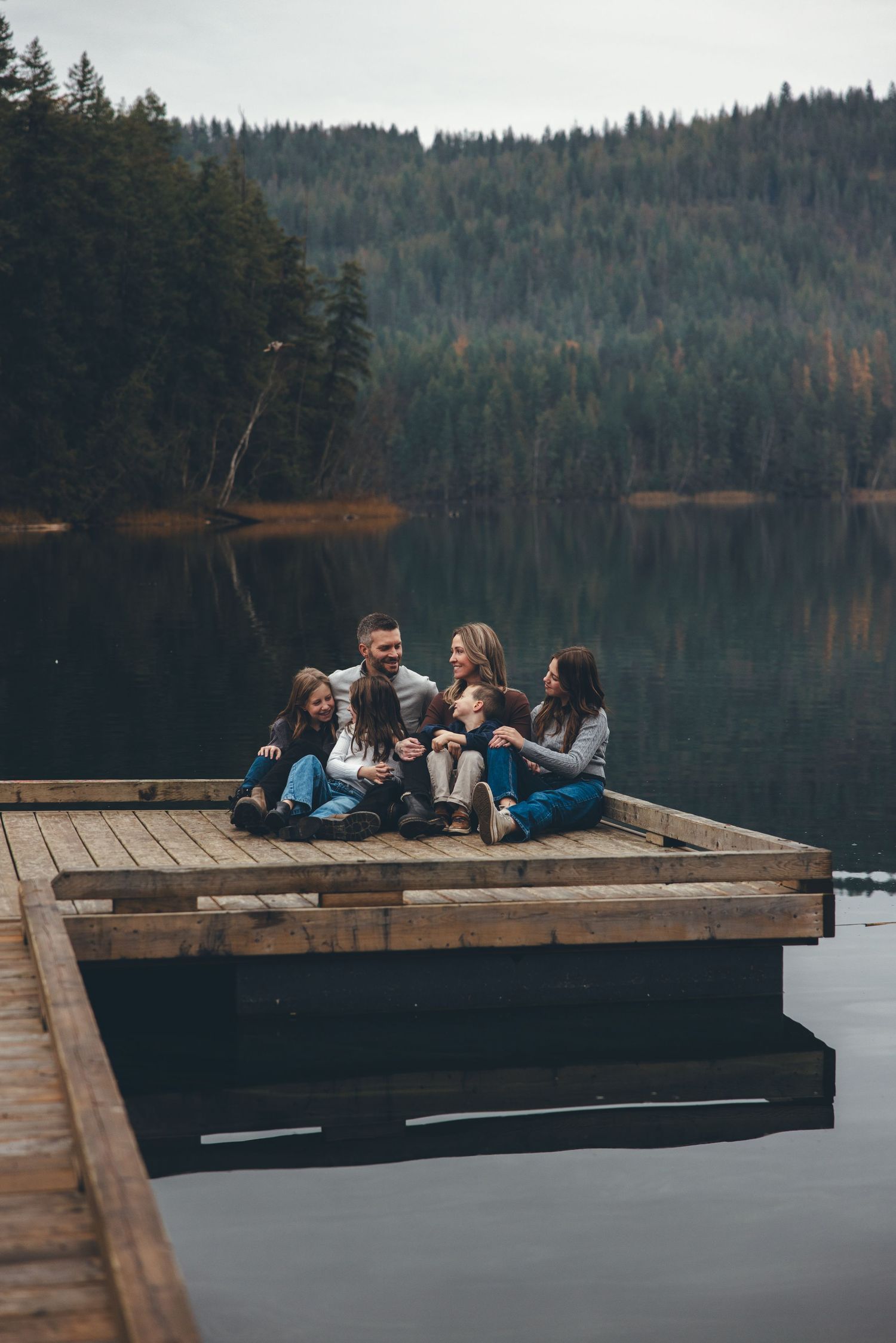 Group relaxing on wooden dock overlooking serene mountain lake surrounded by forest.