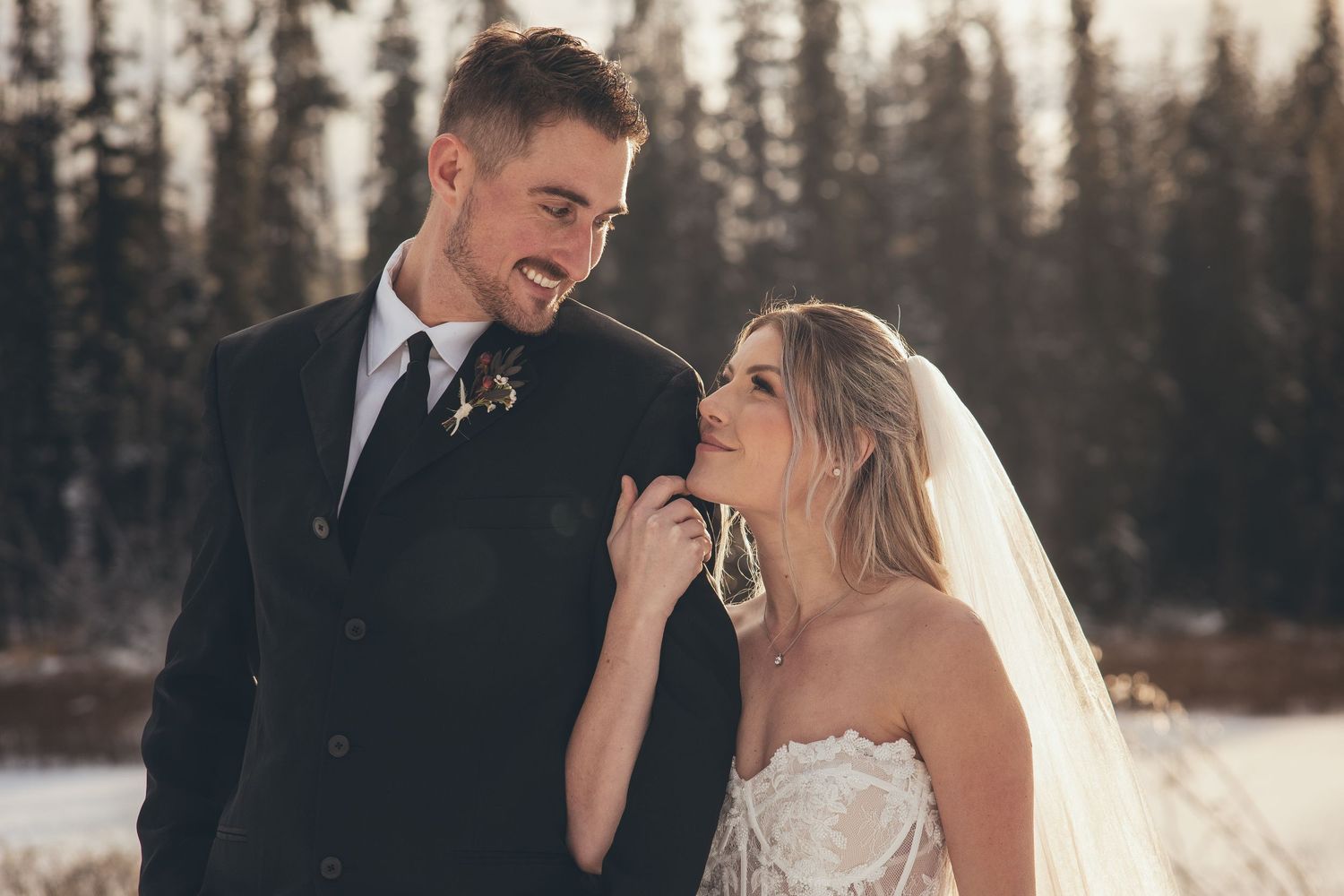 A joyful winter wedding couple embracing outdoors against a snowy forest landscape.