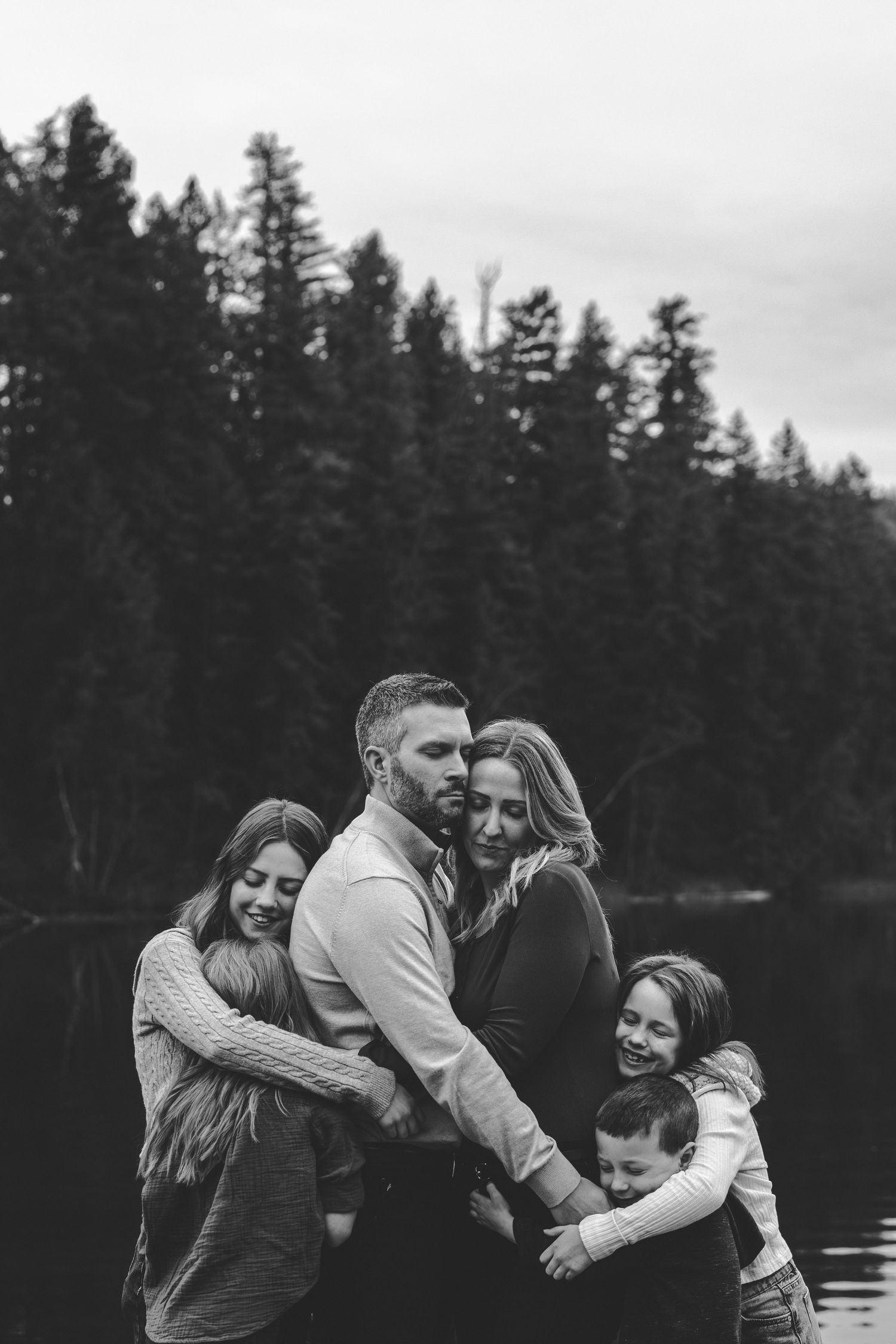 Group sharing joyful embrace on wooden dock by mountain lake.