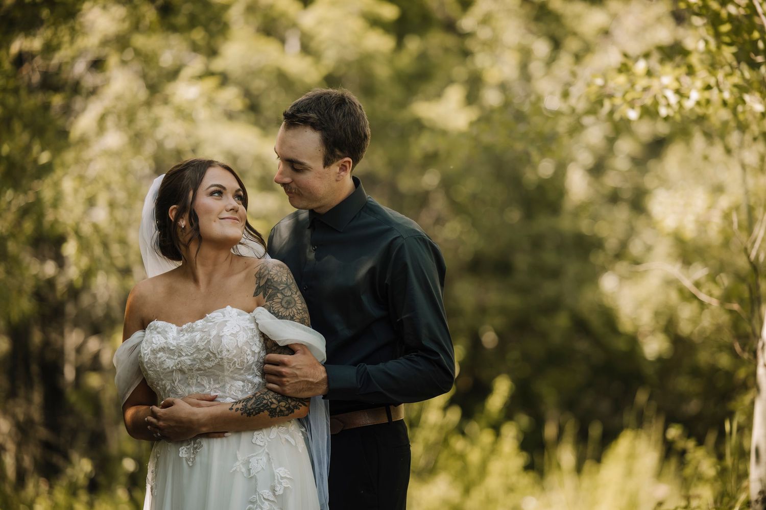 A couple shares tender moments in a sun-drenched field with trees in the background.