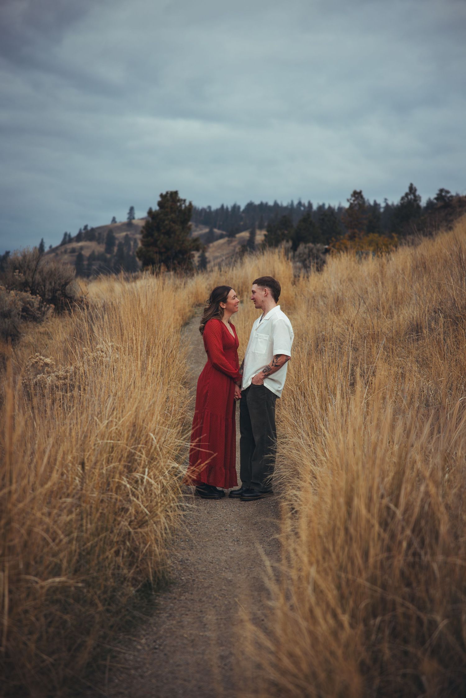 A couple in red and white stand together on a scenic trail surrounded by tall golden grass.