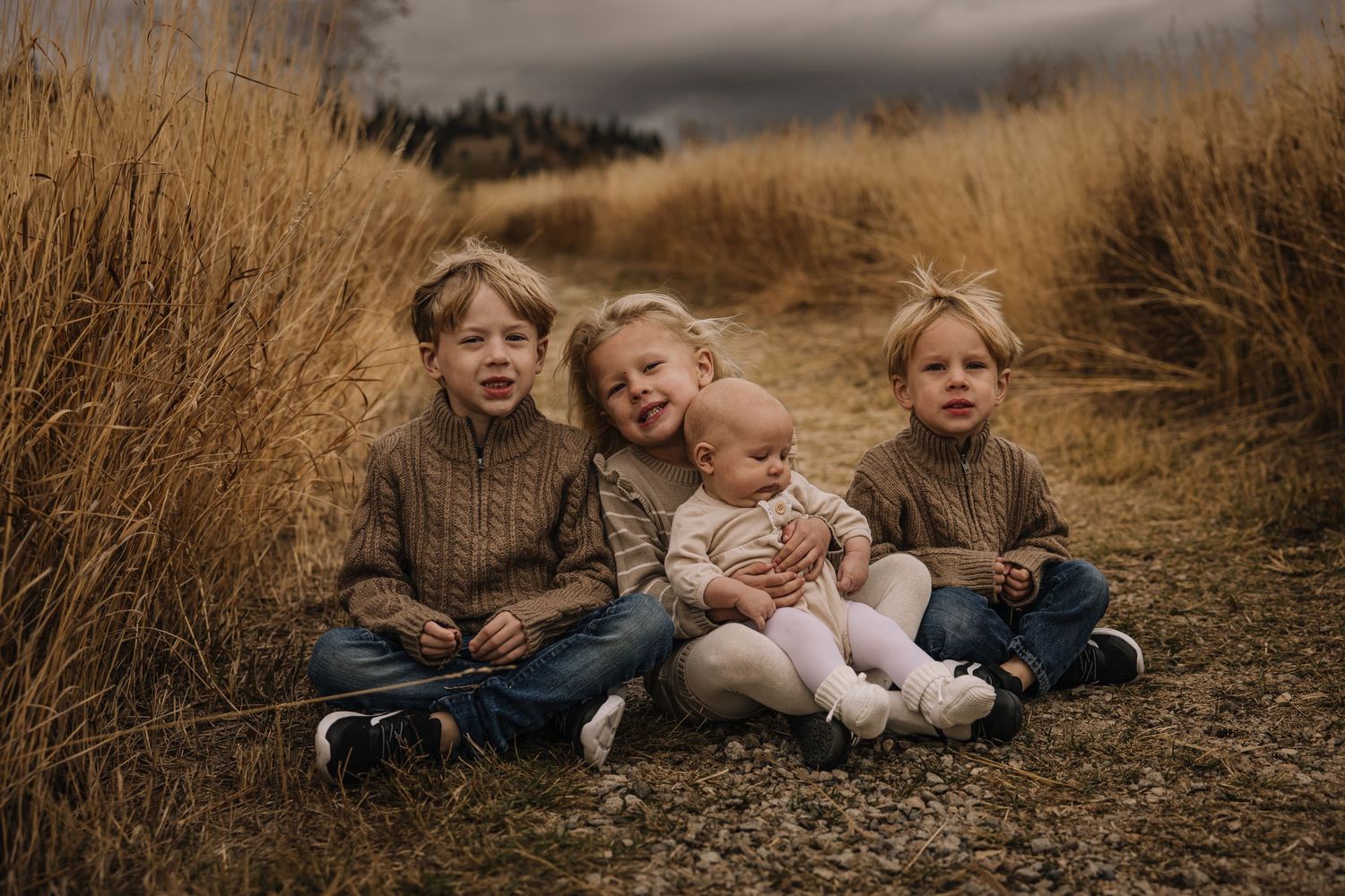 Family relaxing together in tall autumn grass during outdoor photo session.