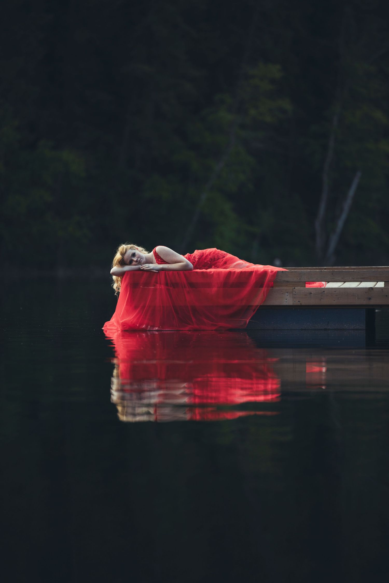 Dramatic red dress reflection mirrored in still lake water at dusk.