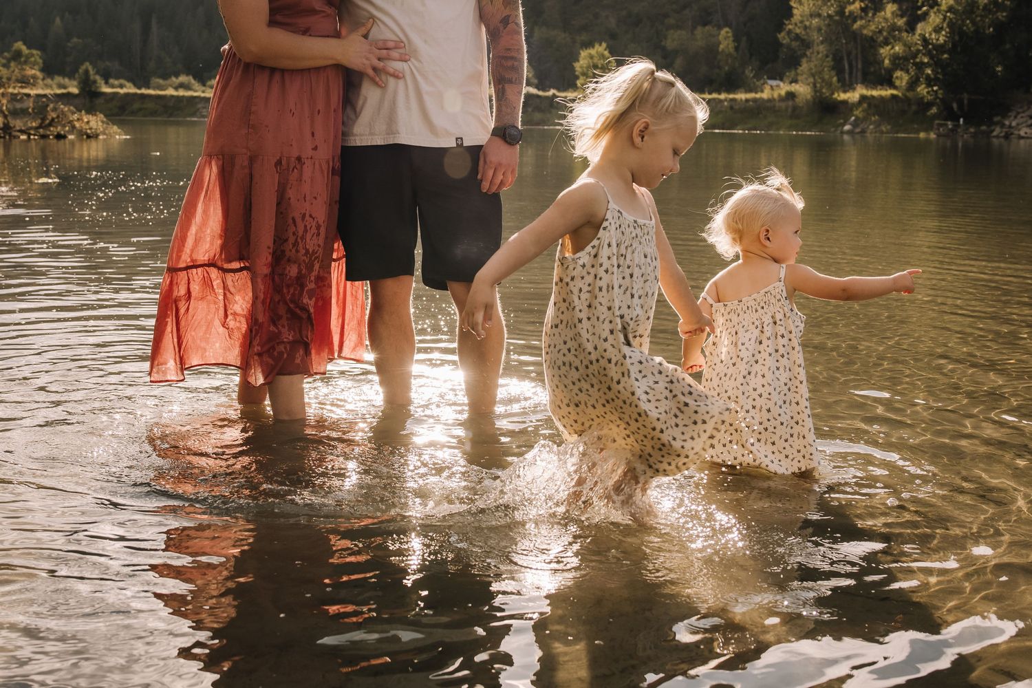 Family playing and splashing in shallow water during sunset at a lake.