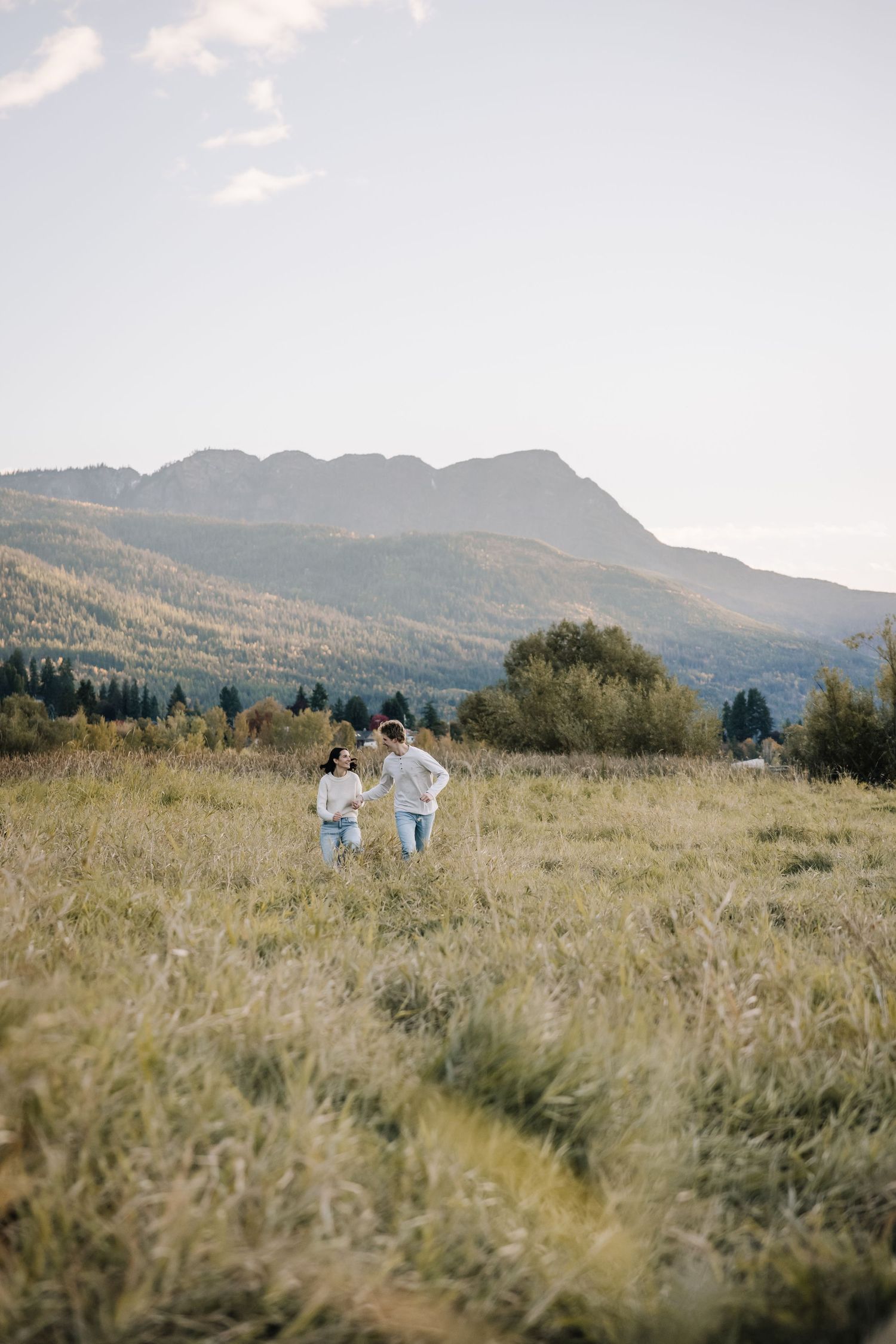 Distant figures walking through a scenic mountain meadow with tall grass and rolling hills.