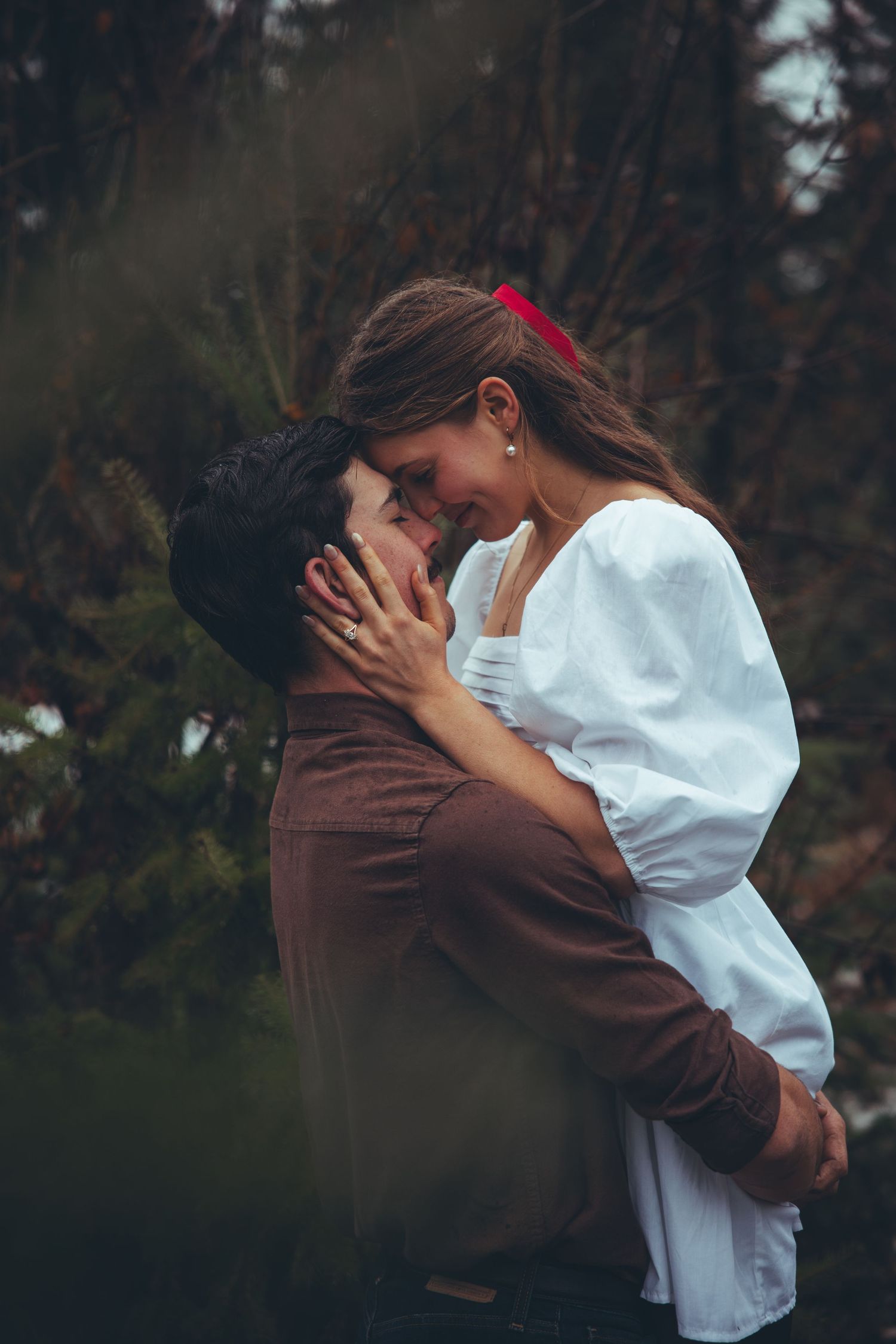 An intimate moment captured against a moody forest backdrop with soft lighting.