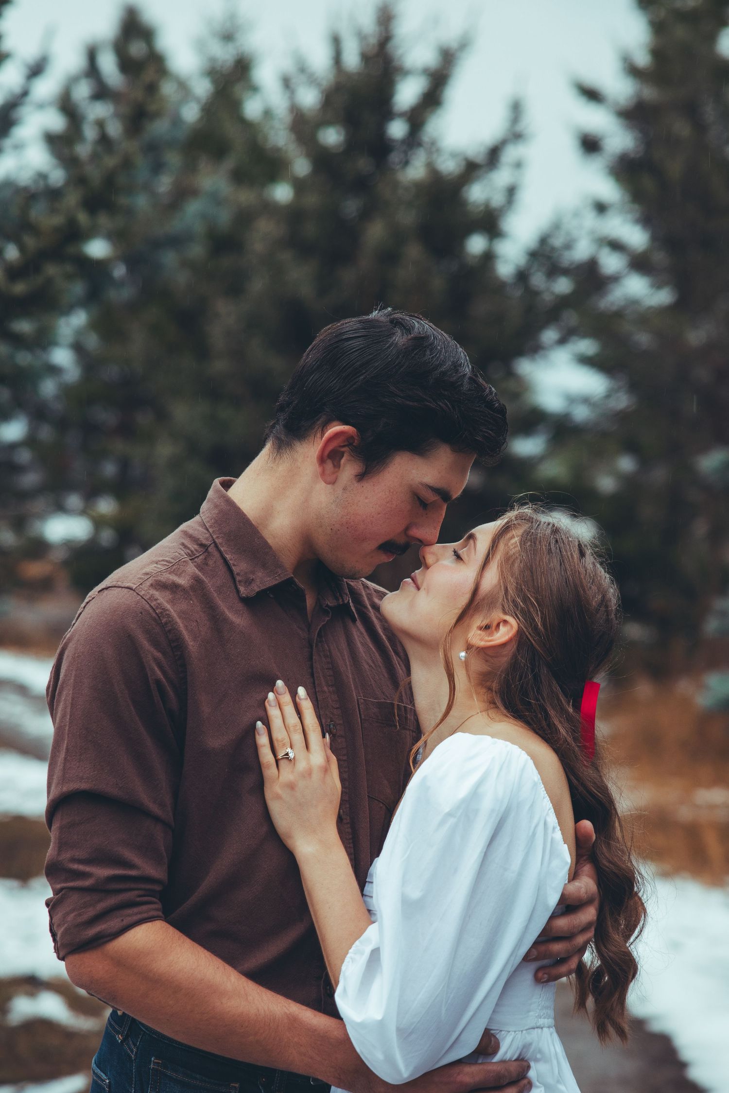 A romantic winter photoshoot in the snow with evergreen trees in the background.