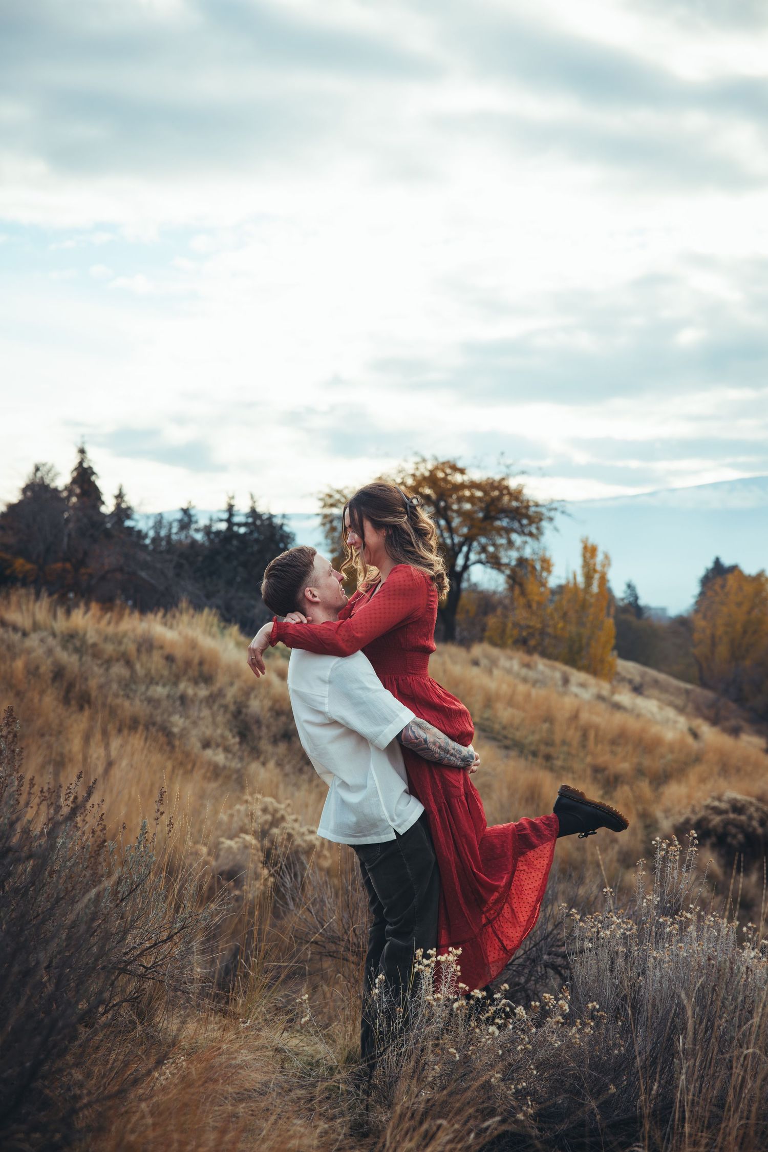 A romantic moment captured in a field with golden grass and cloudy skies.