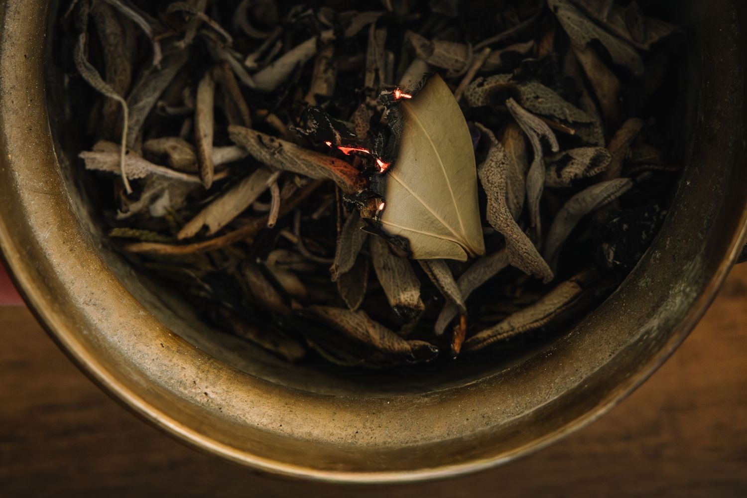 Dried herbs and botanicals in a rustic ceramic bowl photographed from above.
