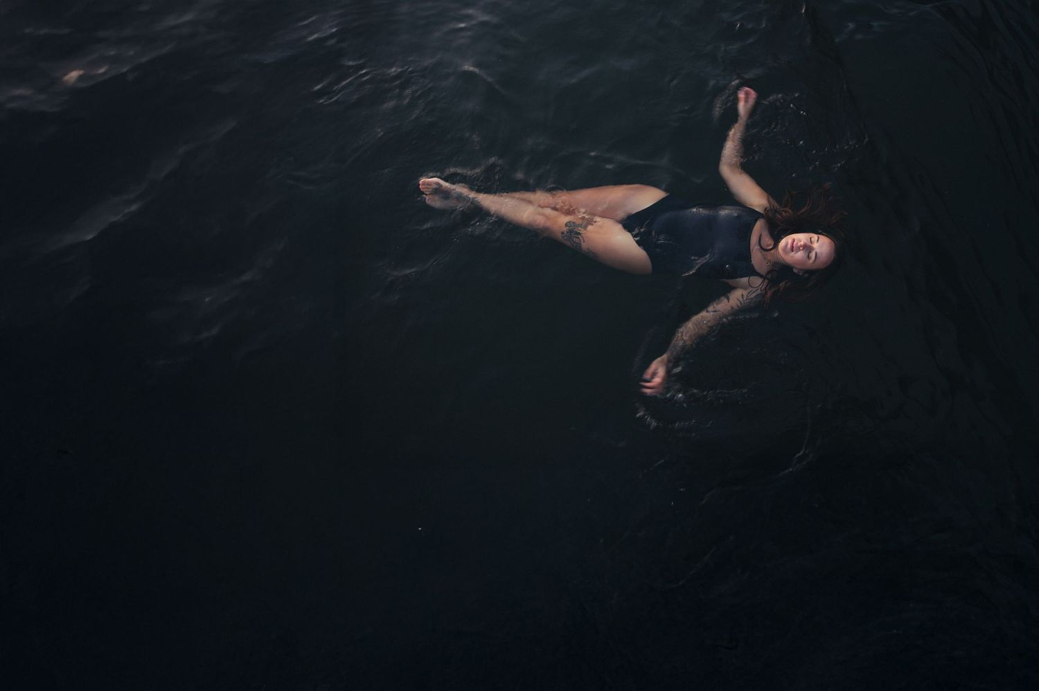 Dark artistic portrait of floating figures in water.