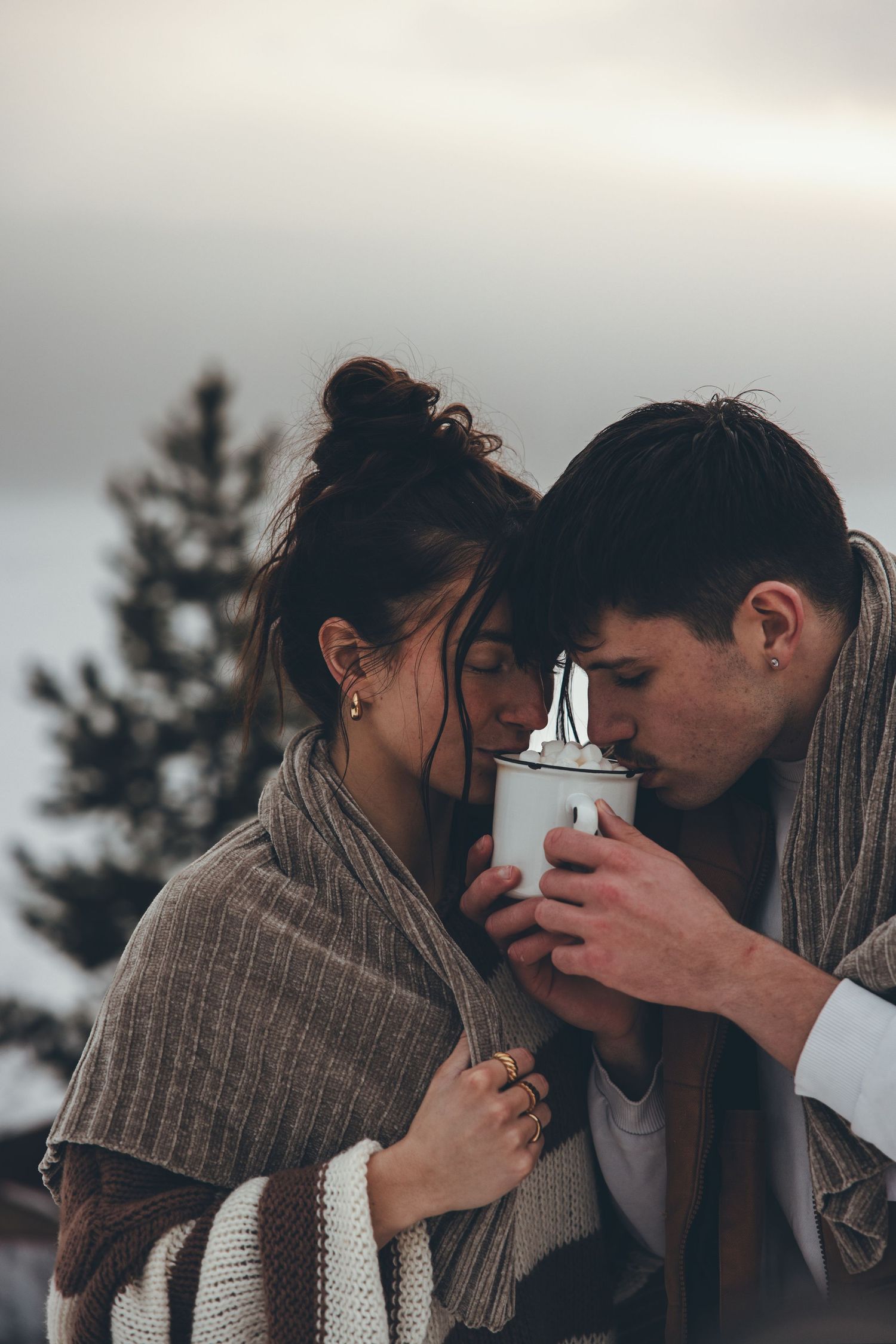 A romantic winter scene with a couple sharing an intimate moment while wearing cozy sweaters against an evergreen backdrop.