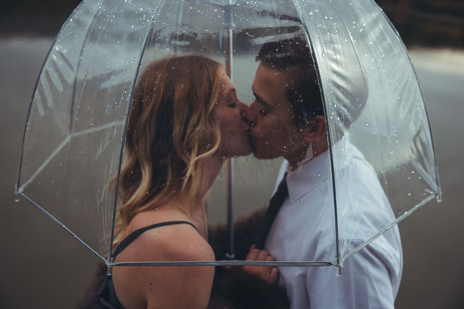 Couple sharing an intimate moment under a clear umbrella on a rainy day.