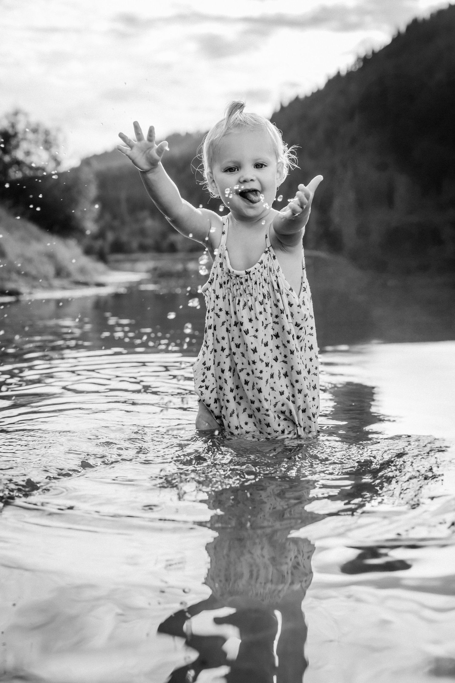 Black and white photo of a child splashing joyfully in lake water.