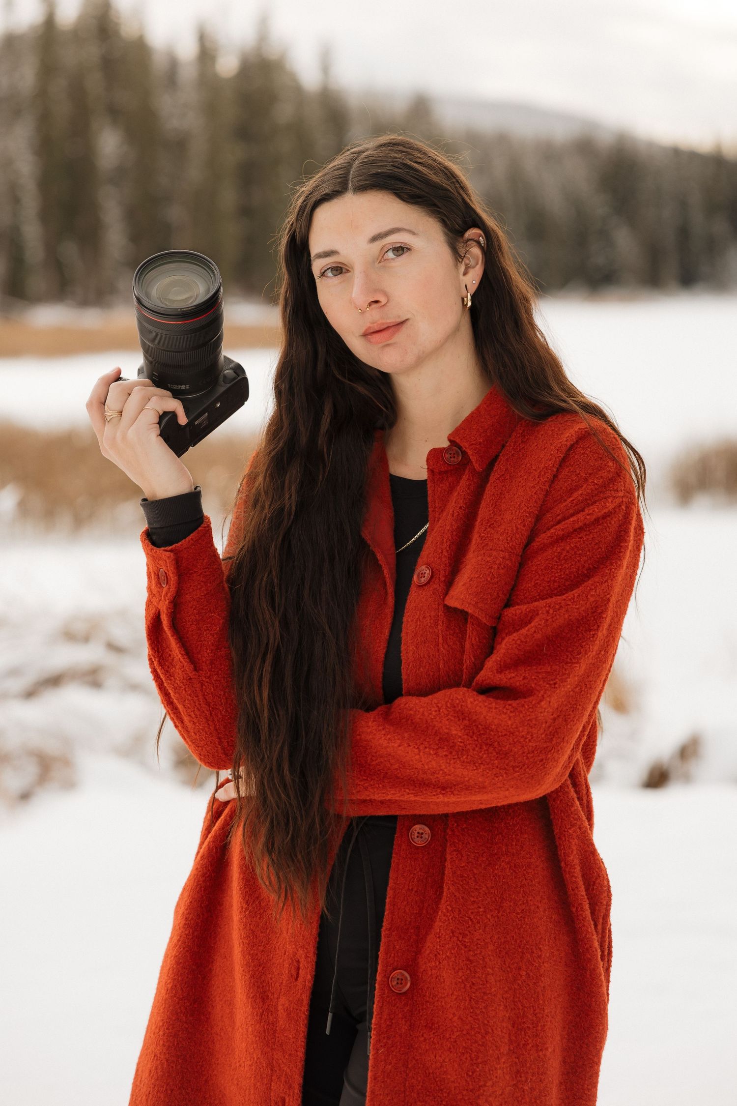 A photographer in a bright red coat holding a camera against a snowy winter backdrop.