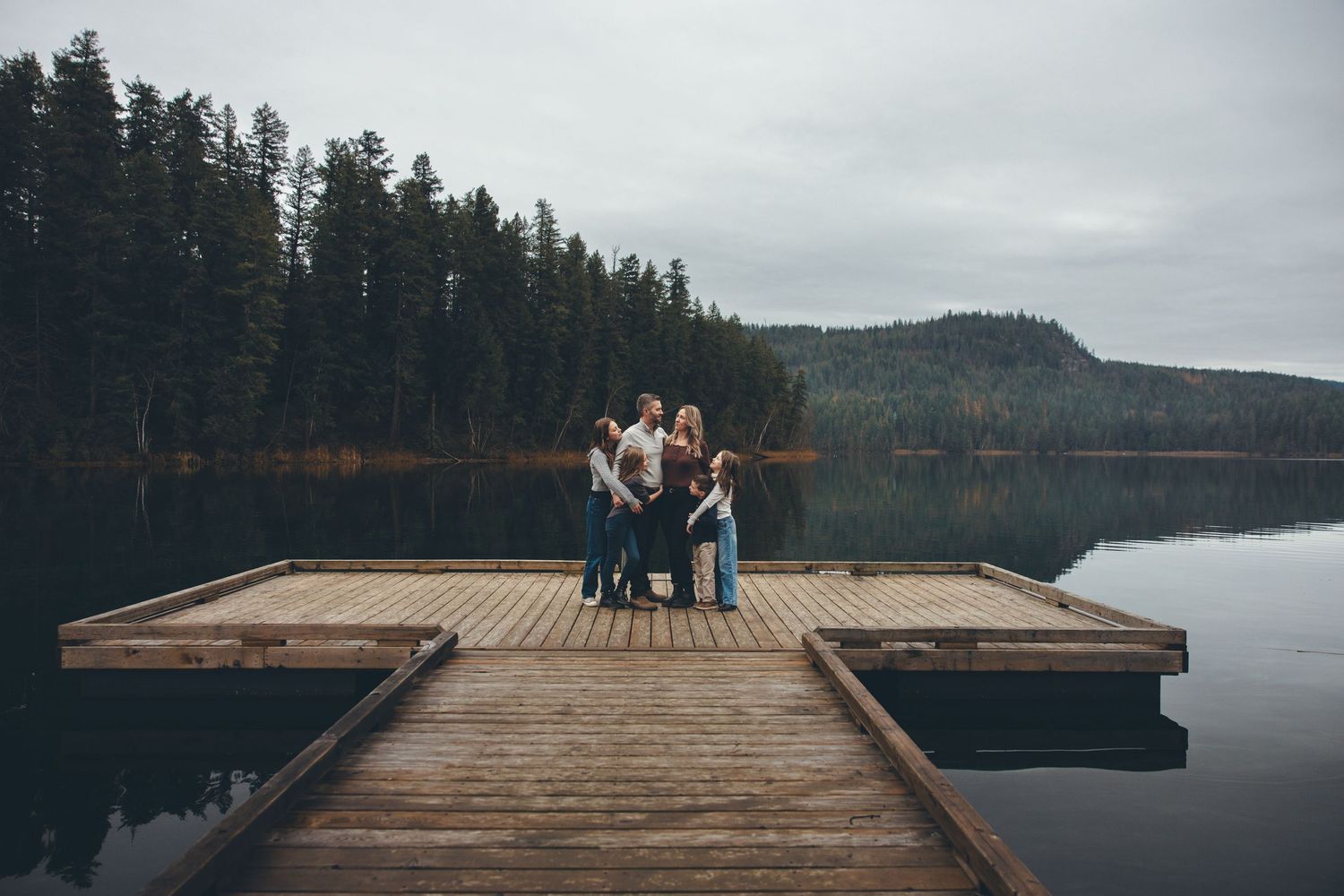 Wide view of wooden dock extending into calm mountain lake with forest backdrop.