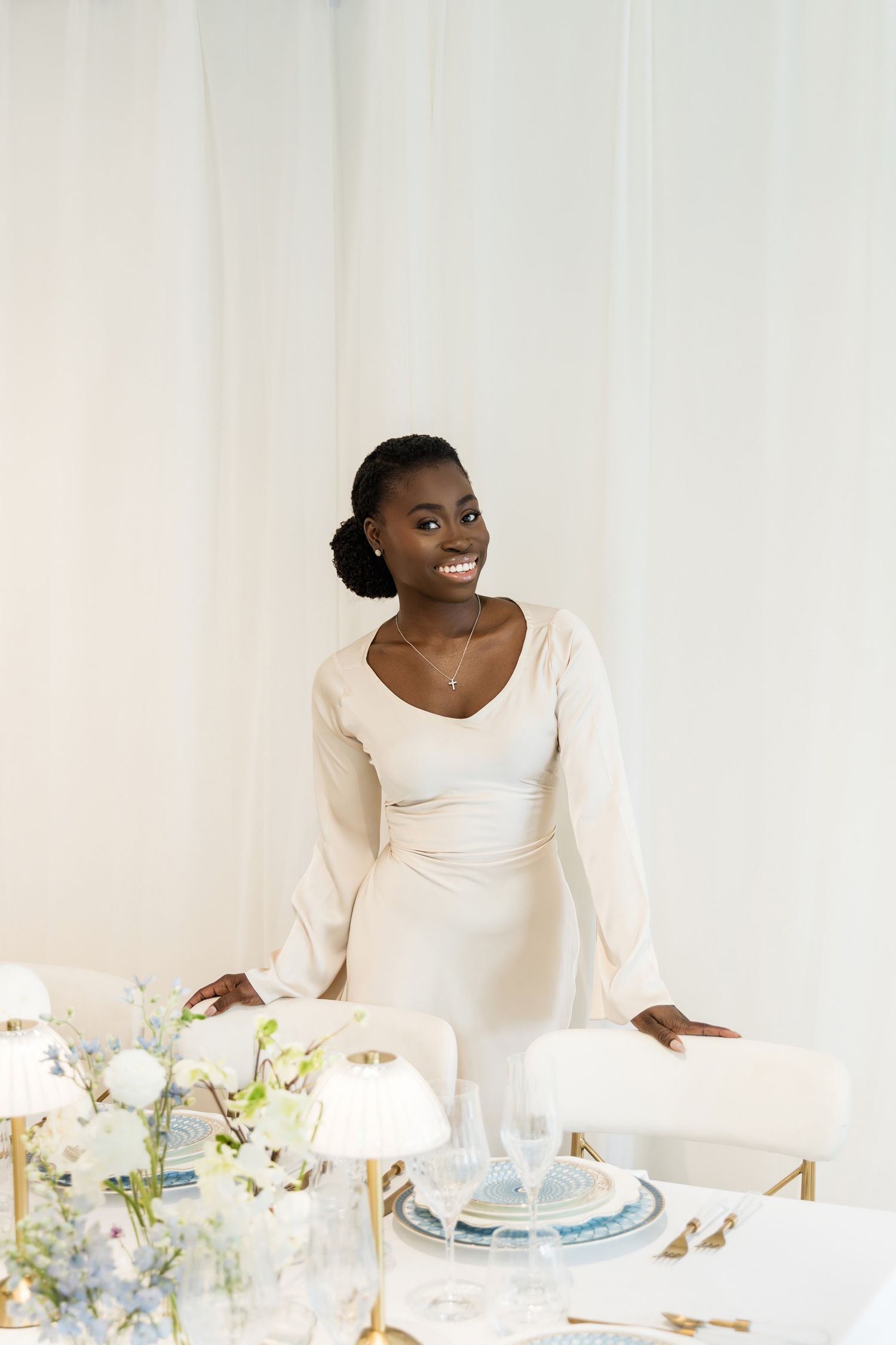 Luxury event planner posing beside an elegant blue and white tablescape with floral arrangements and gold accents in Palm Beach, Florida.