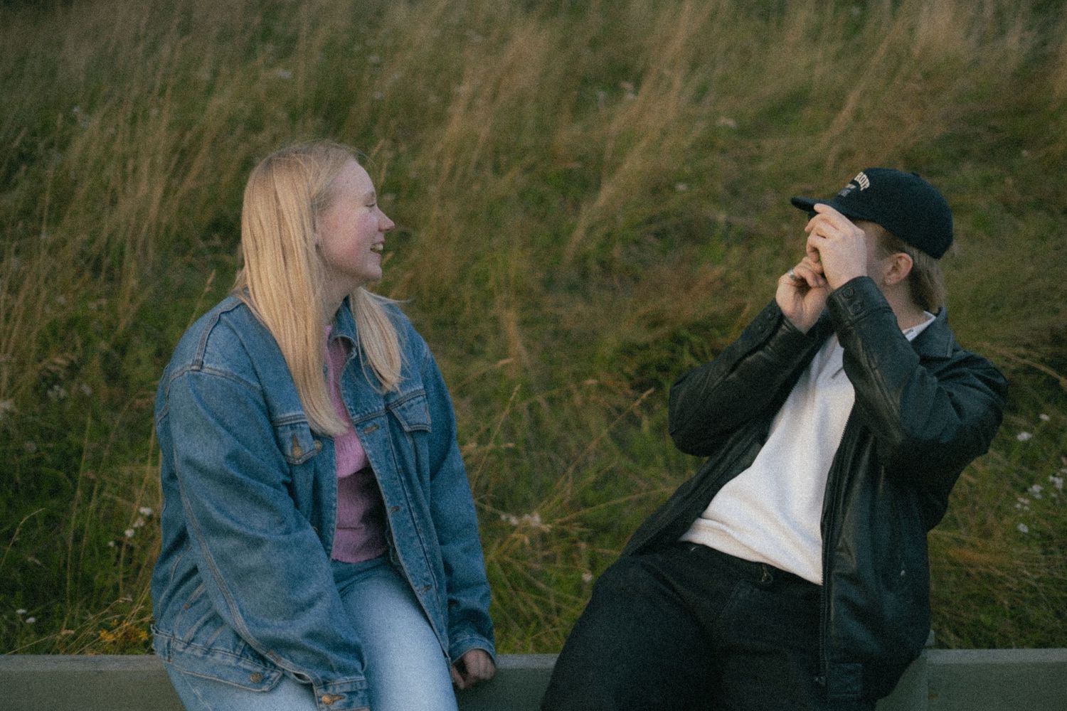 A couple in denim and casual wear share intimate moments while sitting in tall grass during golden hour.