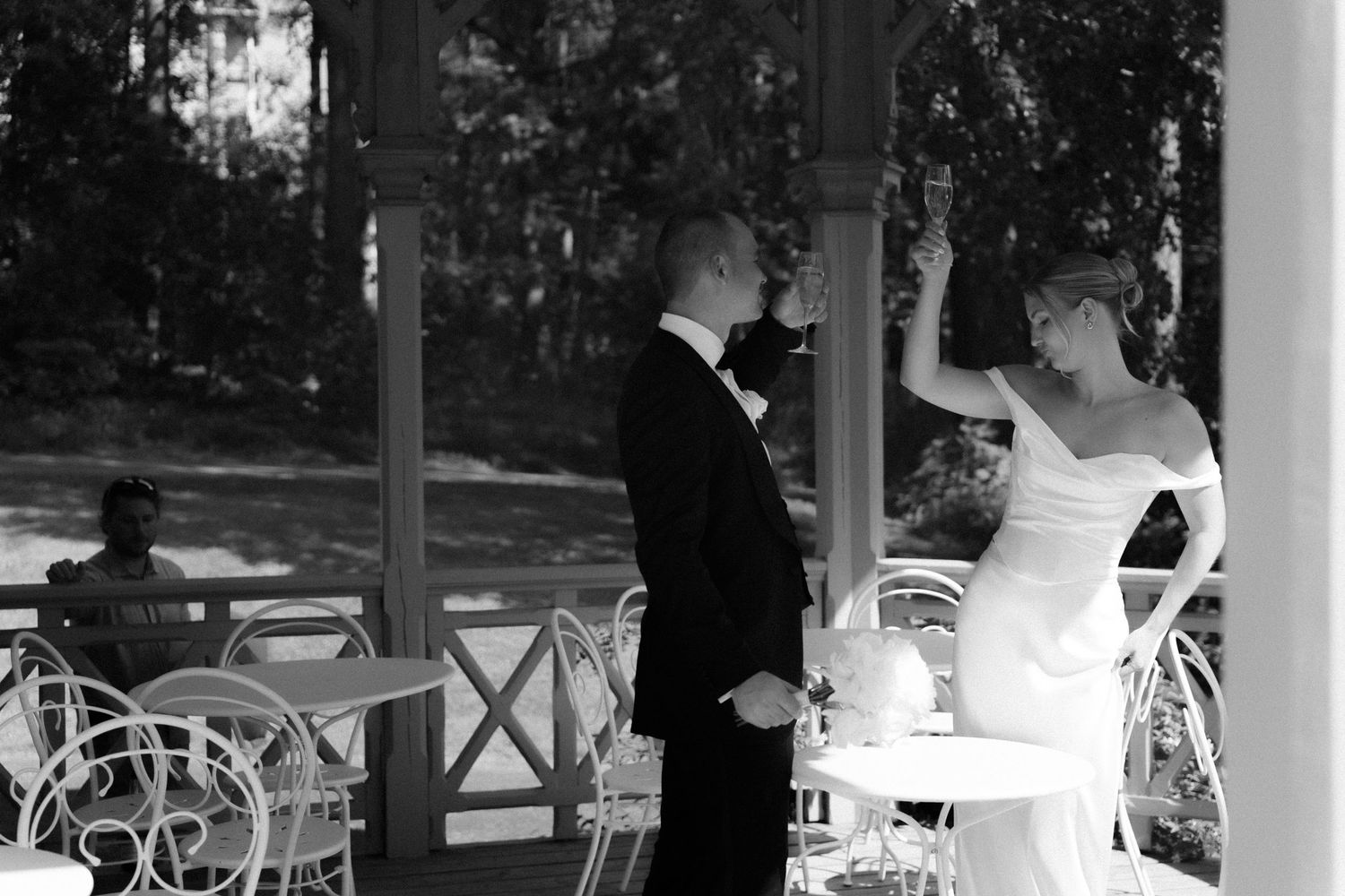 A black and white wedding reception photo showing guests seated at tables under an elegant covered porch.