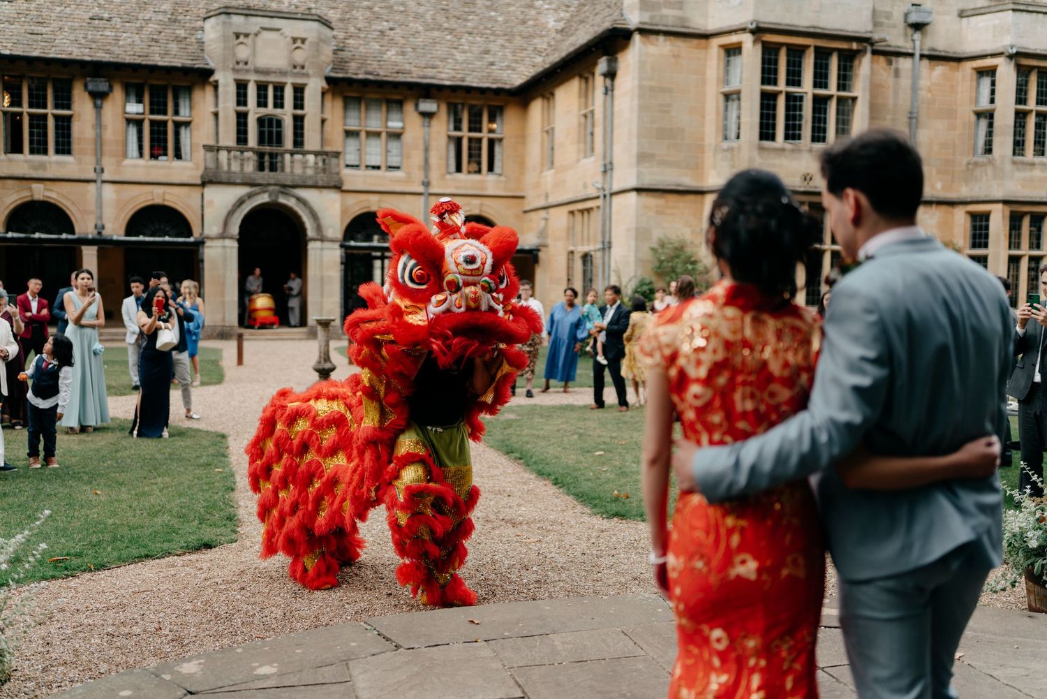 Couple watches a vibrant red Chinese lion dance performance at an elegant outdoor wedding celebration.