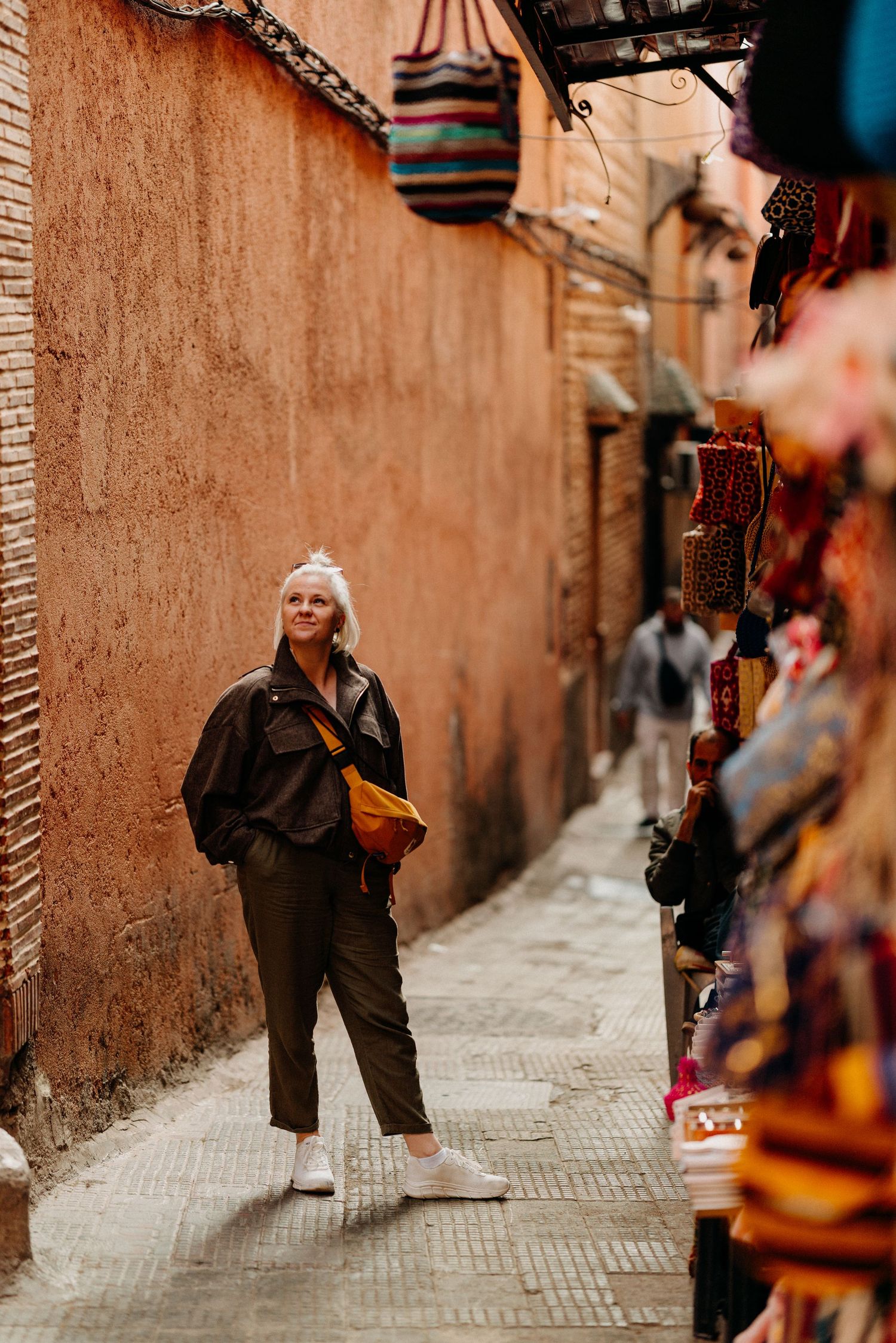 Woman with white hair explores colorful narrow market alley in the ancient medina of Marrakech.