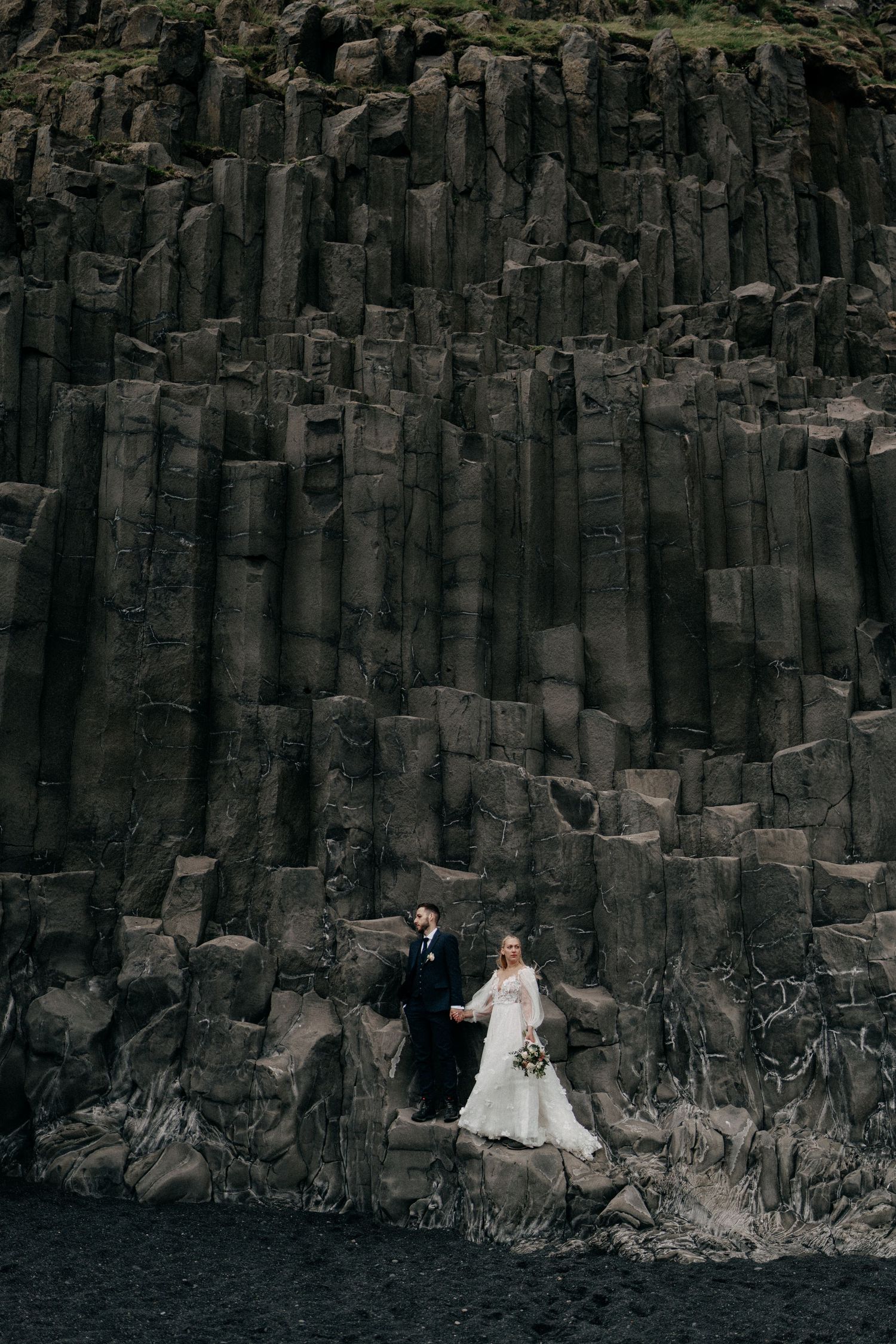 Wedding couple standing on dramatic black basalt columns at Reynisfjara beach in Iceland.