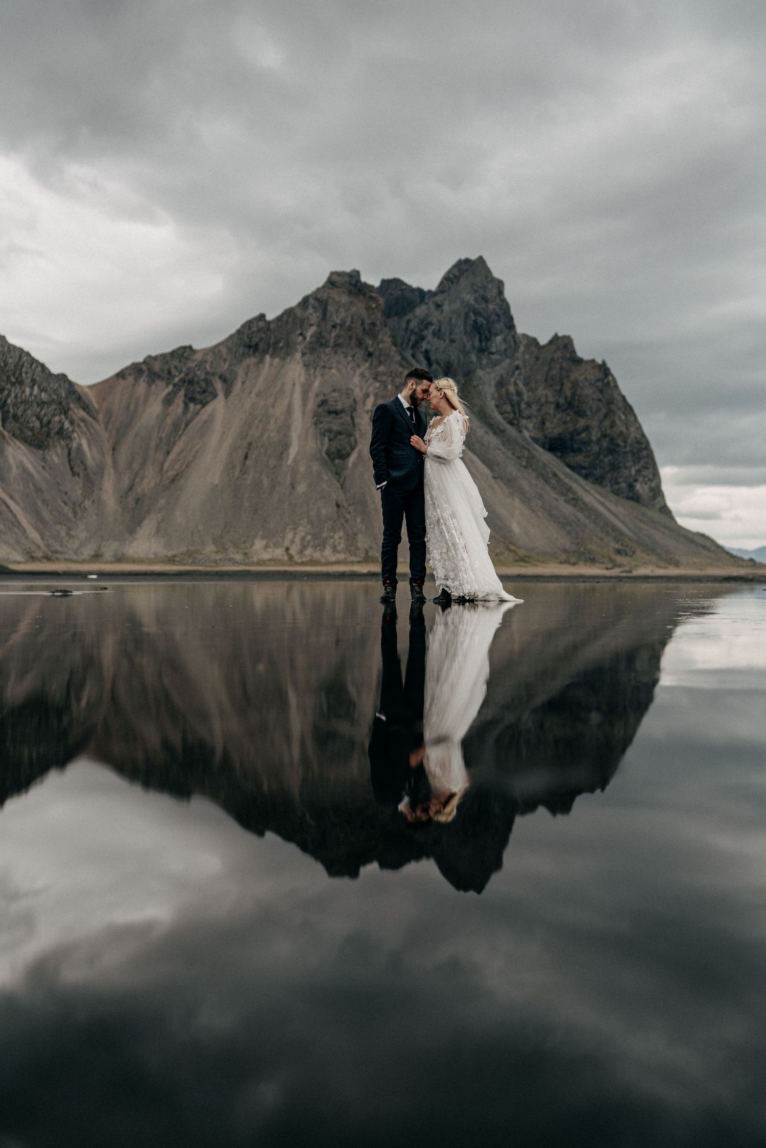 Bride and groom kissing with stunning mountain reflection on still water in Iceland elopement.