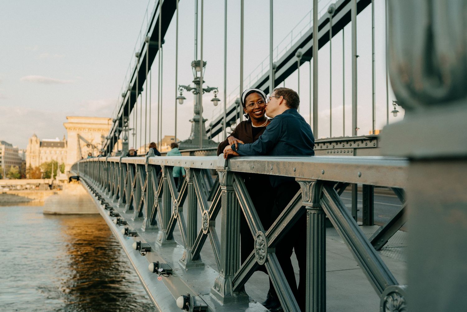 A couple shares a romantic moment on the Chain Bridge in Budapest at sunset.