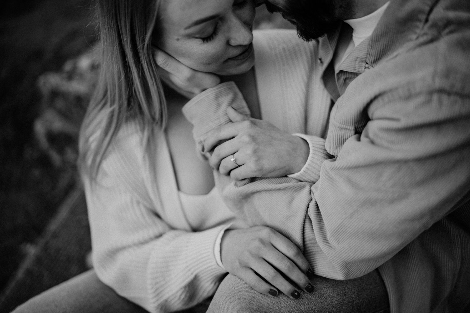Black and white close-up of couple embracing tenderly, hands intertwined, in an intimate engagement photo.