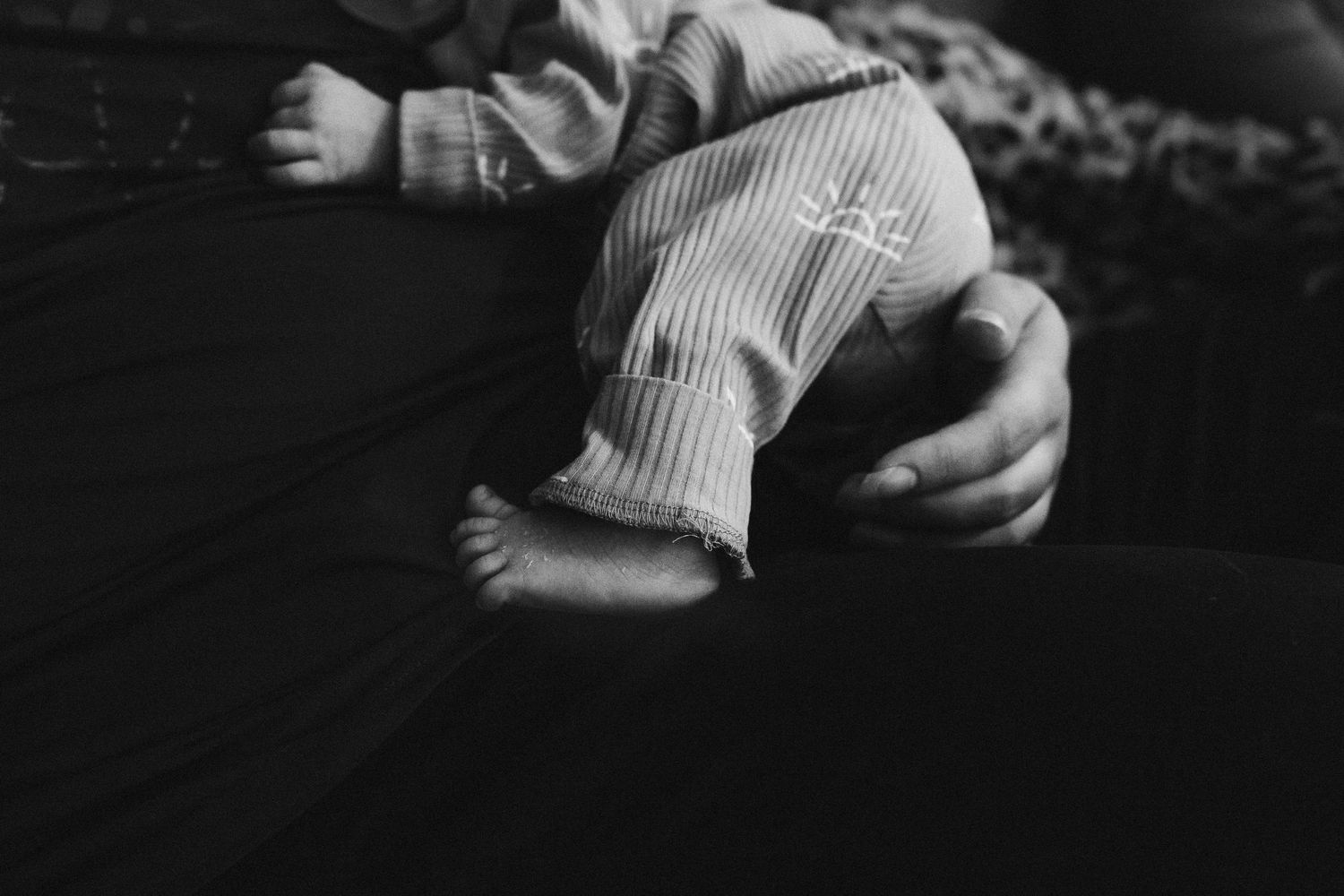 Black and white: Close-up of baby's hand and foot peeking out from clothes as he rests on mom
