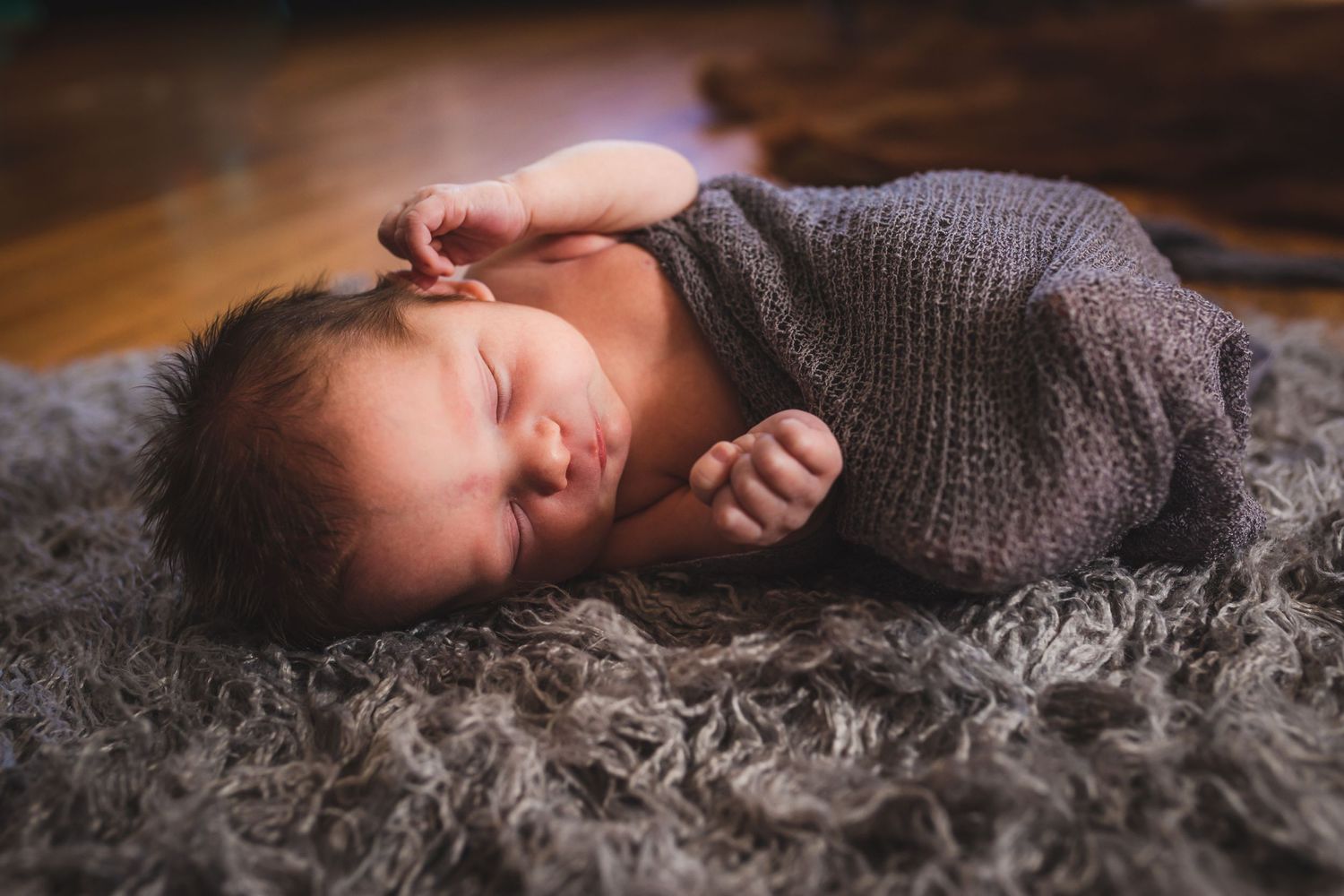 Newborn swaddled in grey wrap, lying on side on shaggy grey carpet