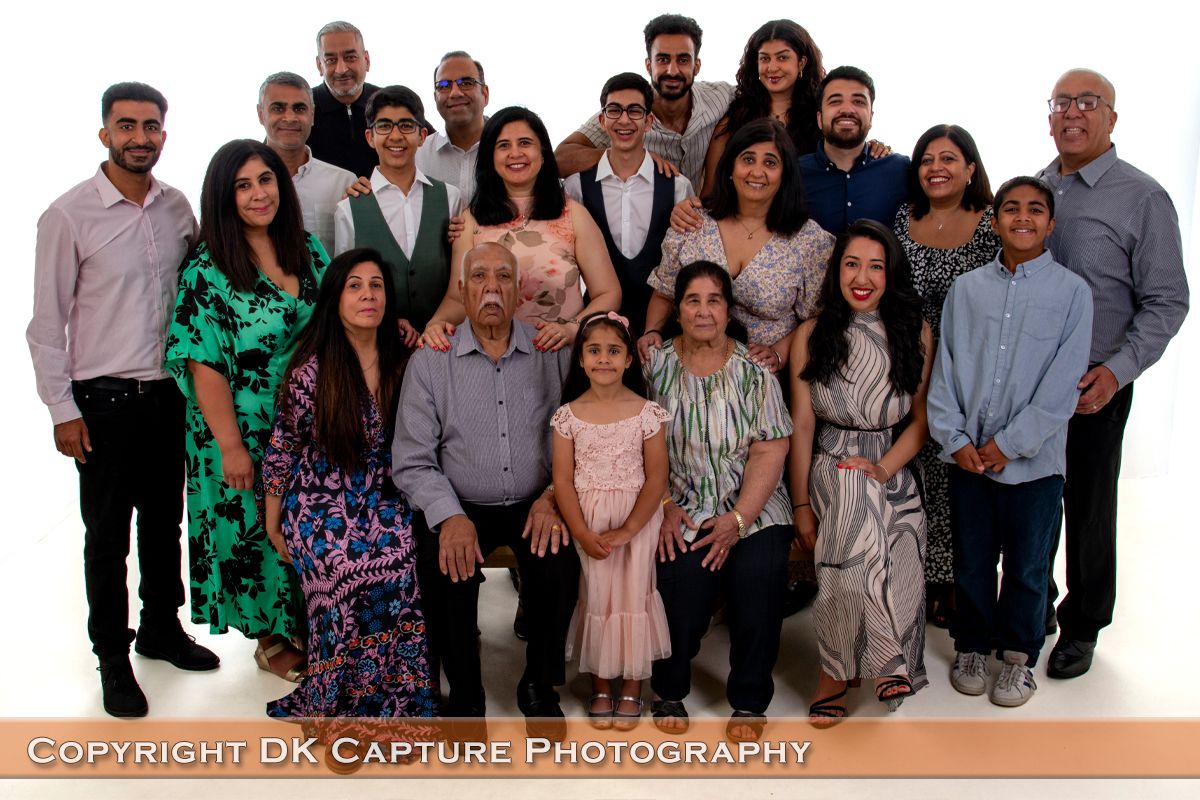 A large family group poses together in coordinated outfits against a plain backdrop for a formal portrait photograph.
