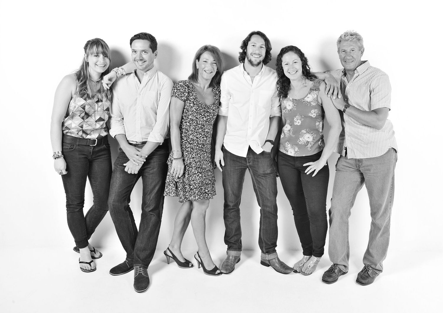 A black and white panoramic group photo shows people sitting and kneeling in casual poses against a white background.