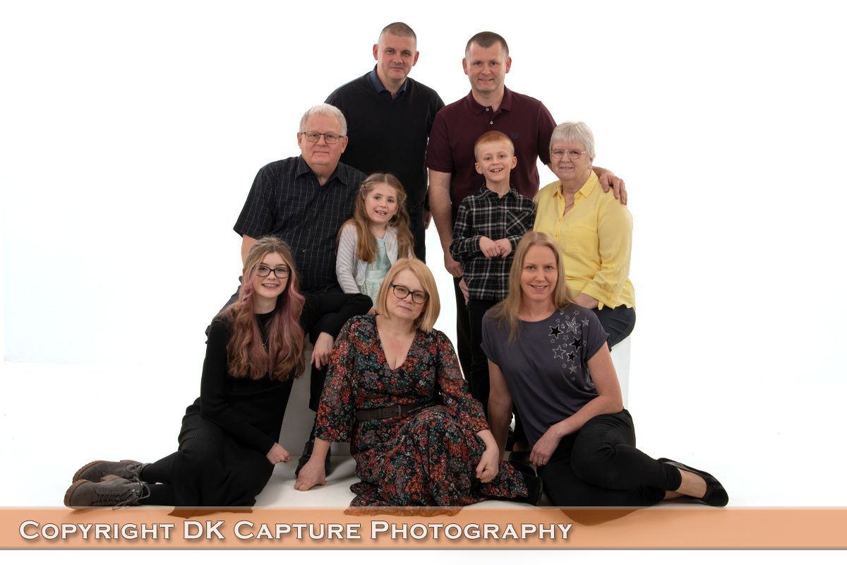 A multi-generational family wearing black and yellow poses together against a white backdrop for a professional portrait.
