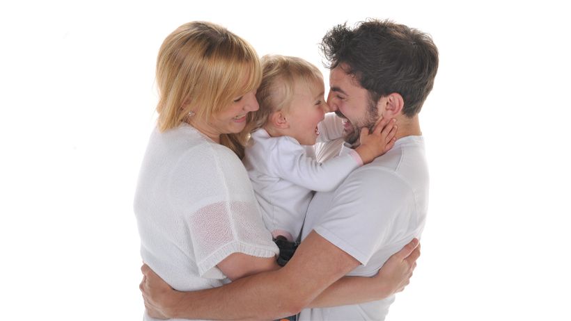 Happy young family with parents holding smiling baby together against white background.