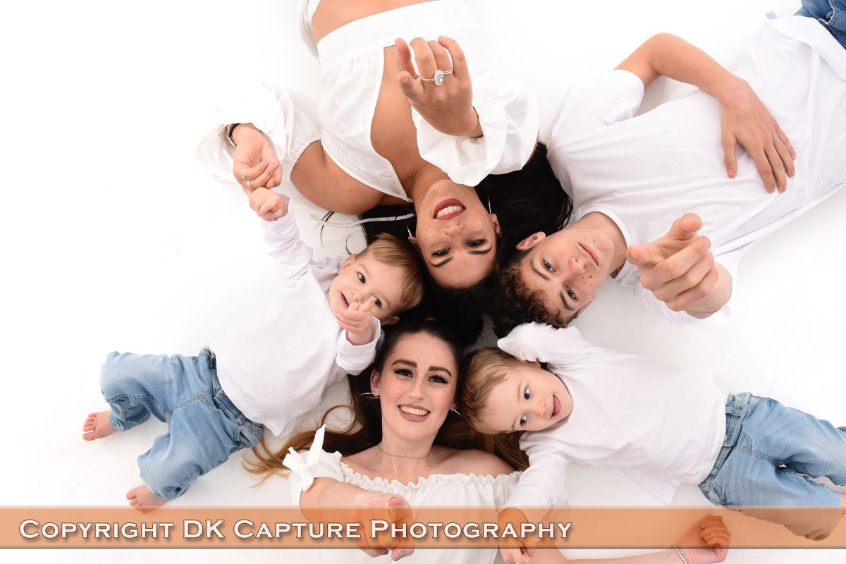 Fun group portrait shot from above of people lying on white background with heads together in circular formation.