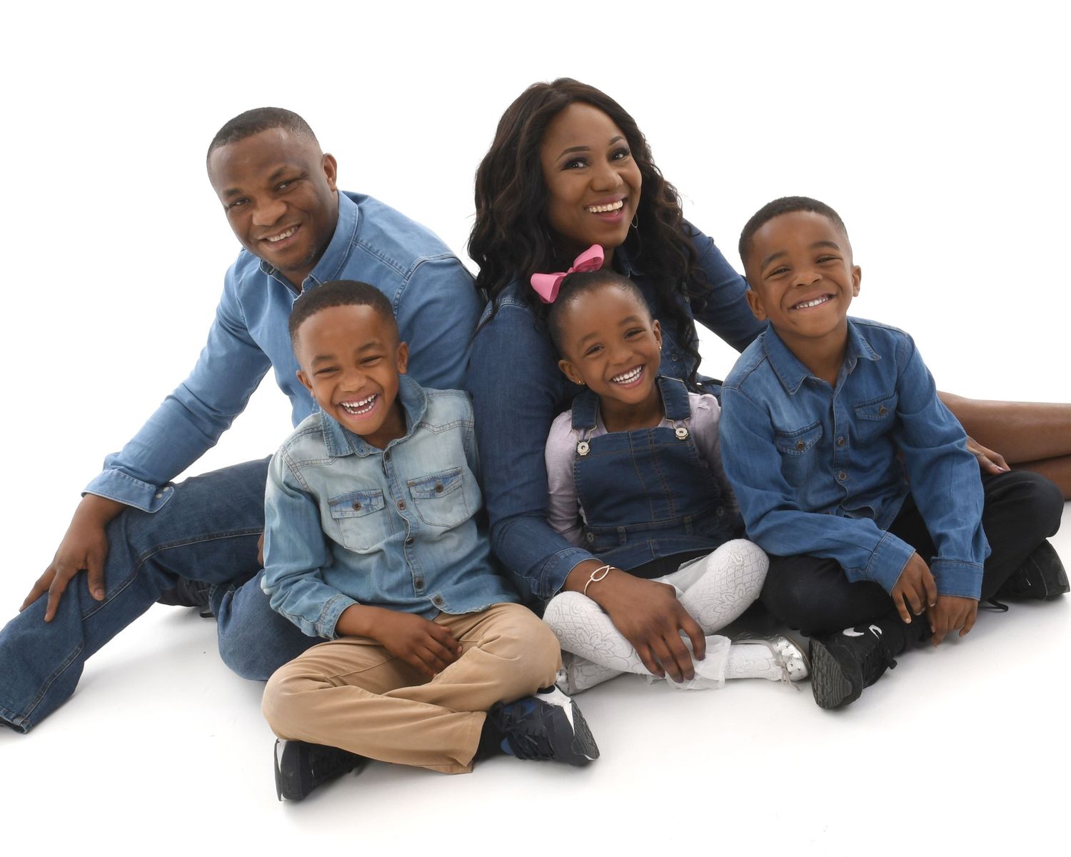 A group of people wearing matching denim outfits lie down in a row on a white background.
