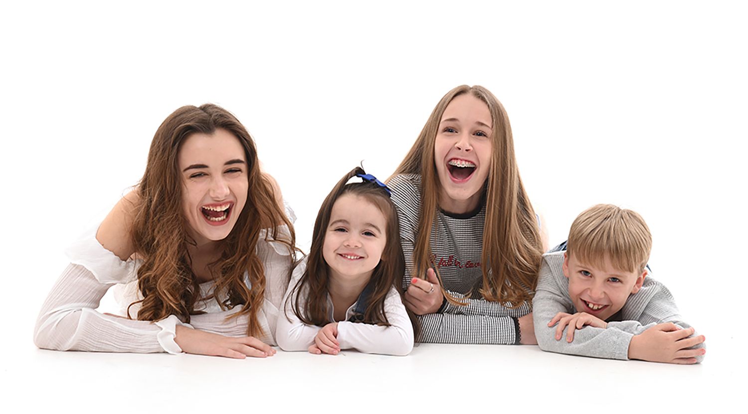 Four happy children laughing and posing together on a white background, radiating joy and sibling bond.