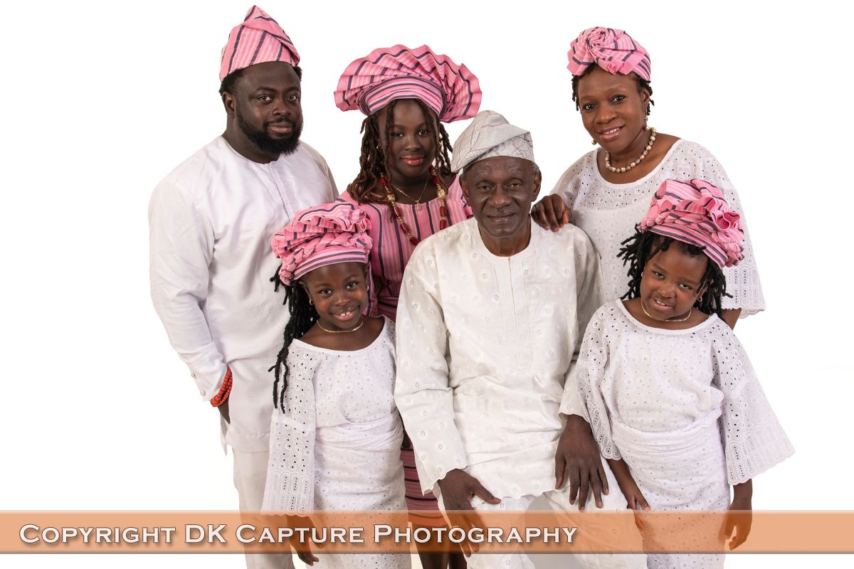 A family wearing coordinated white and pink African traditional attire poses for a formal studio portrait.