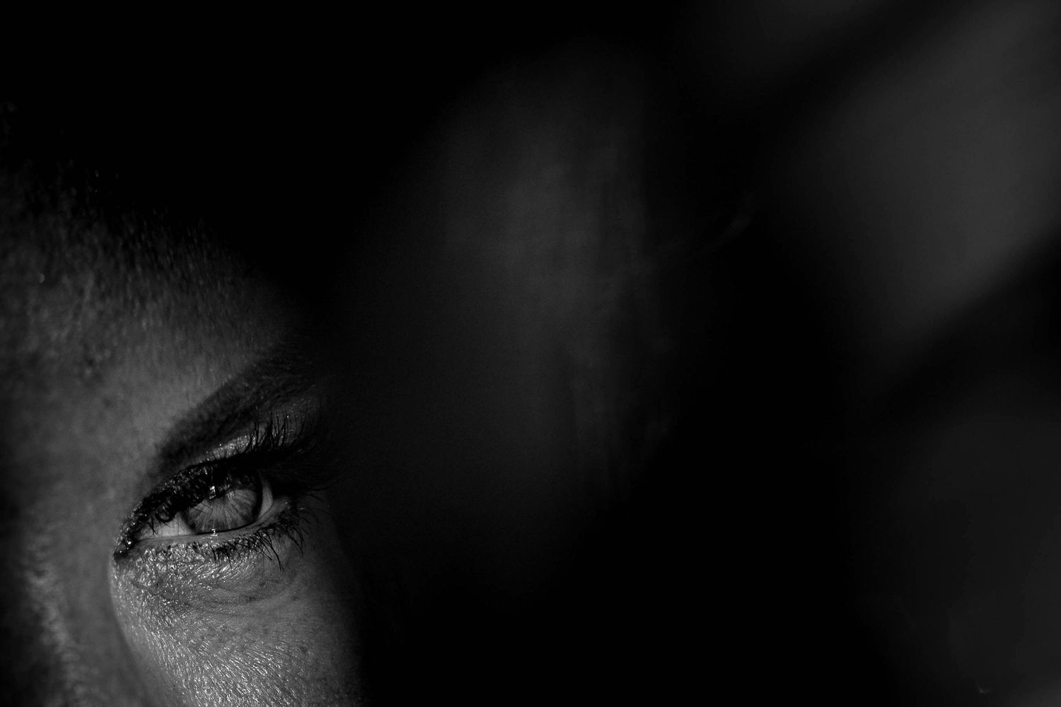 Close-up black and white macro portrait showing a woman's eye with dramatic lighting and deep shadows.