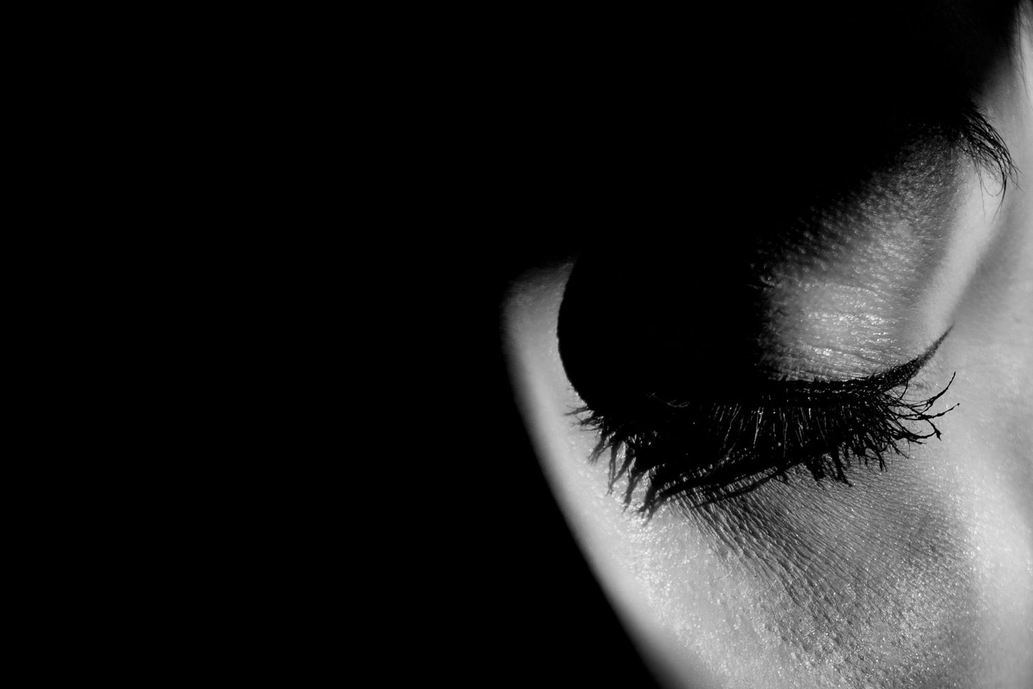 Black and white close-up photo of an eye with dramatic shadows and long eyelashes.