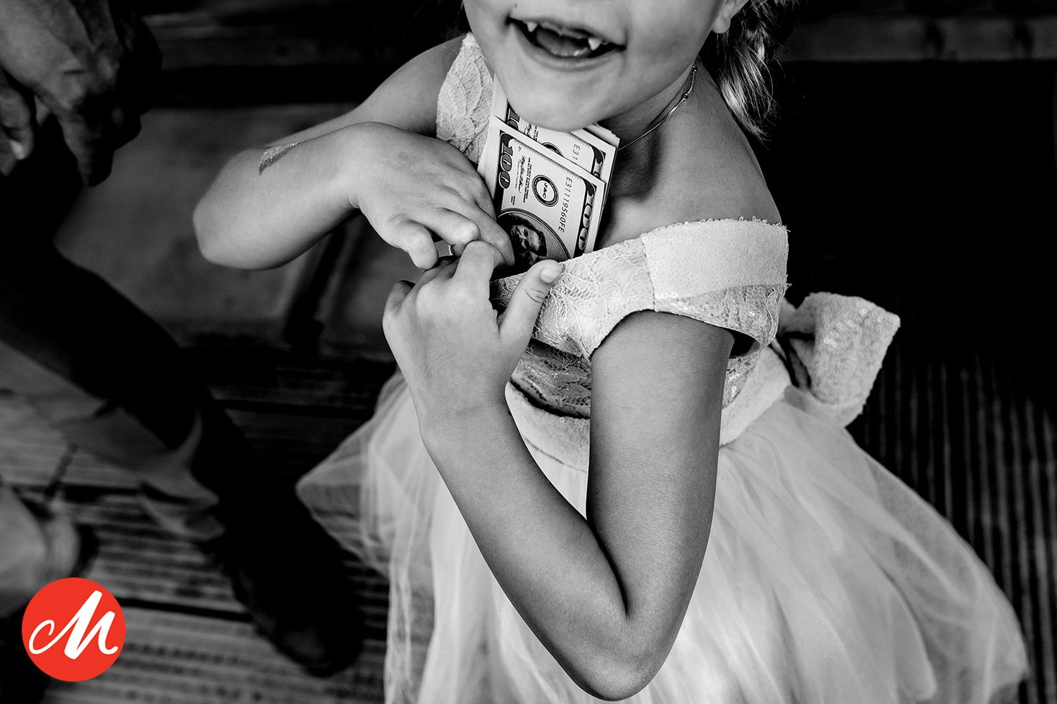A child in a fancy white dress holds a dollar bill while caught in a playful moment at a celebration.