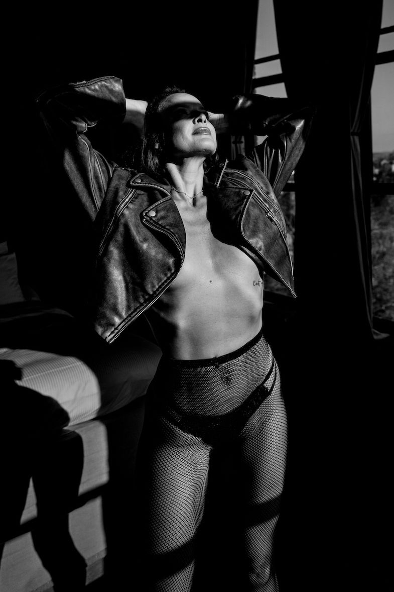 A dramatic black and white artistic photo of an edgy fashion model wearing a leather jacket and fishnet stockings.