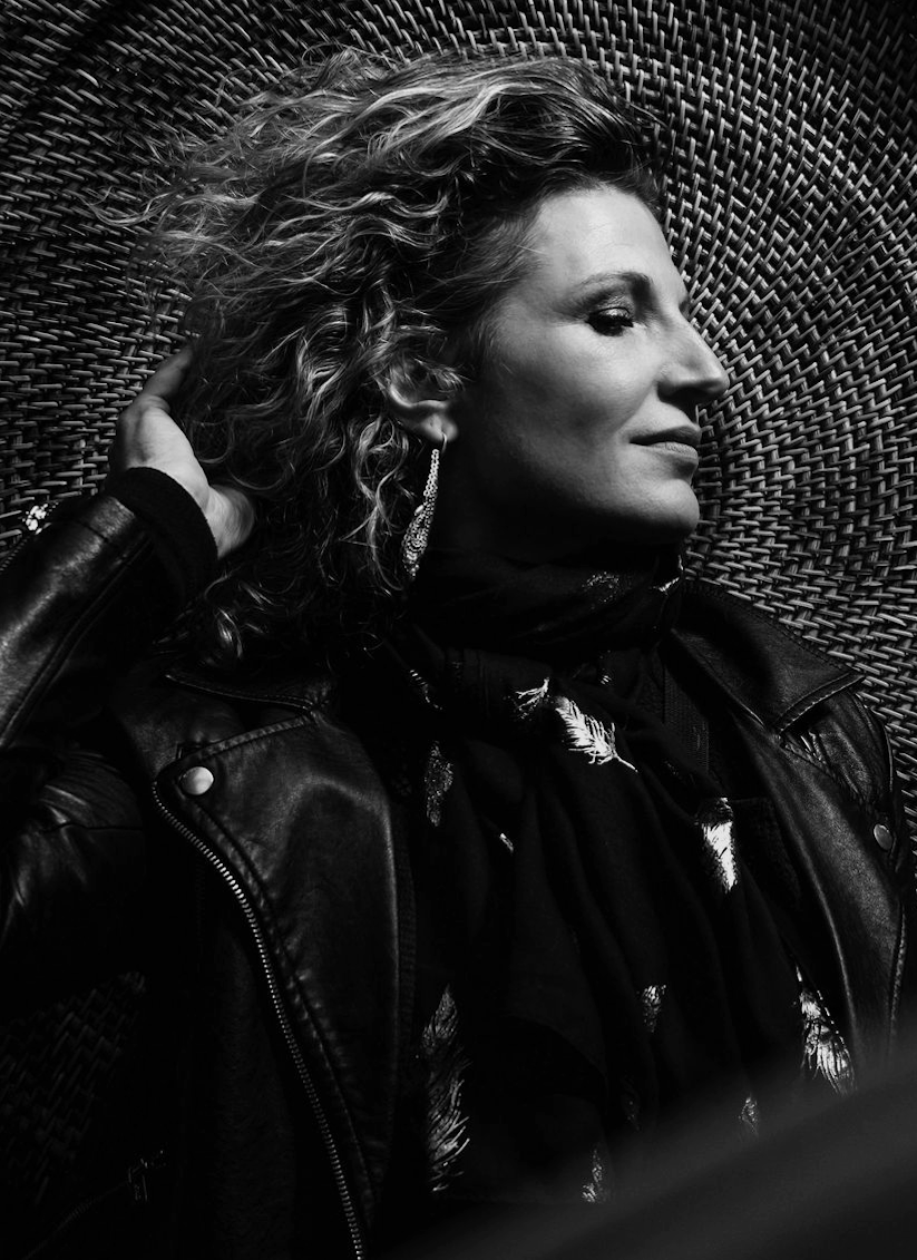 Black and white portrait of a woman in a leather jacket with curly hair and feather earrings.