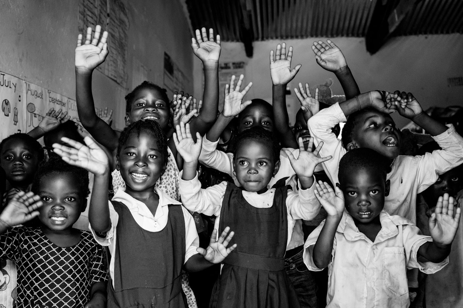 Black and white photo of African schoolchildren joyfully raising their hands in a classroom.