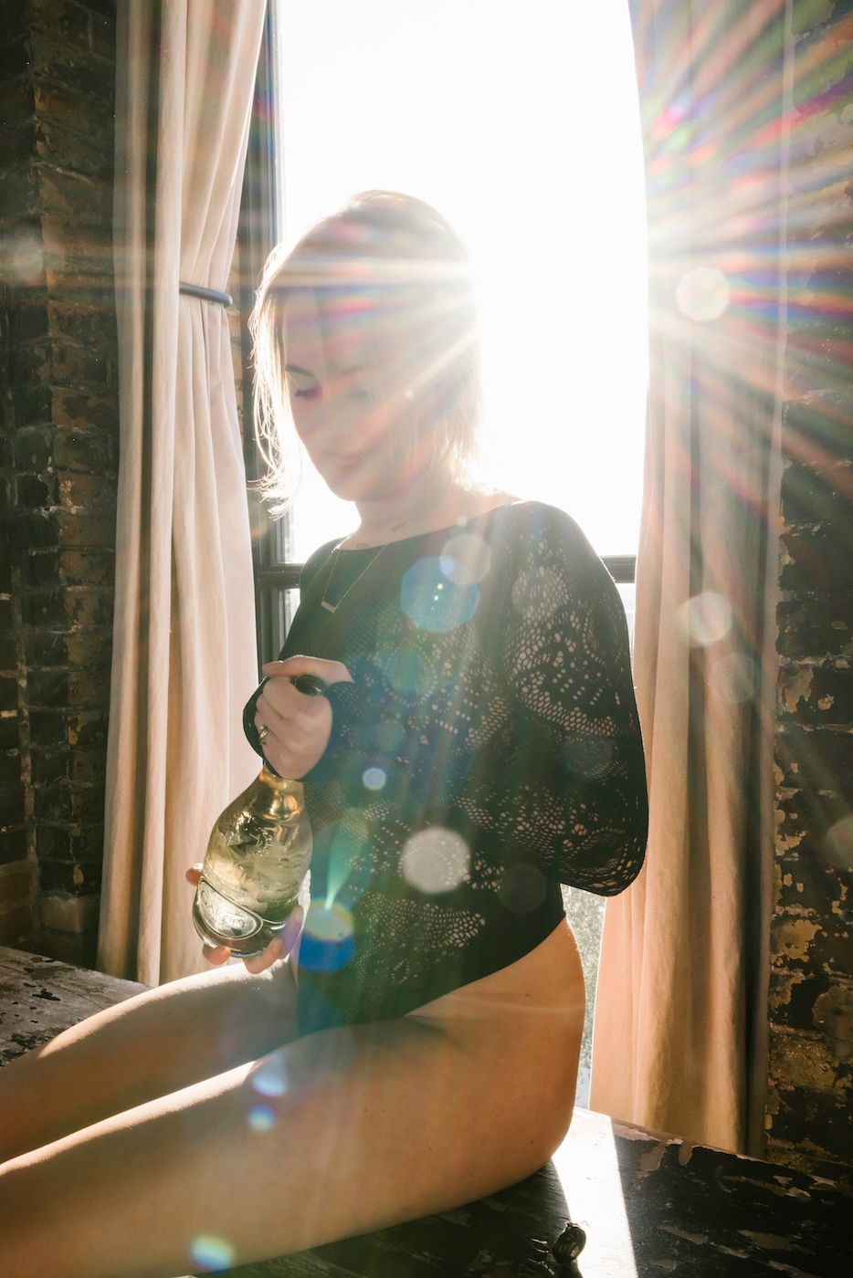 Sunlight streams through window behind silhouetted figure sitting on ledge with cup in vintage brick interior.