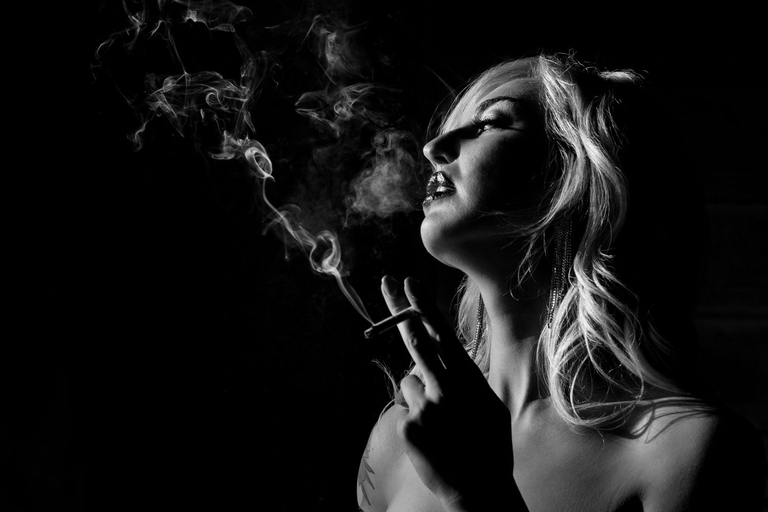 Artistic black and white portrait of someone exhaling smoke against a dark background in dramatic lighting.