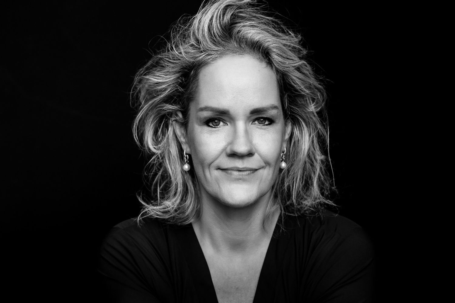 Black and white professional portrait of a smiling blonde woman wearing a black top, studio photography.