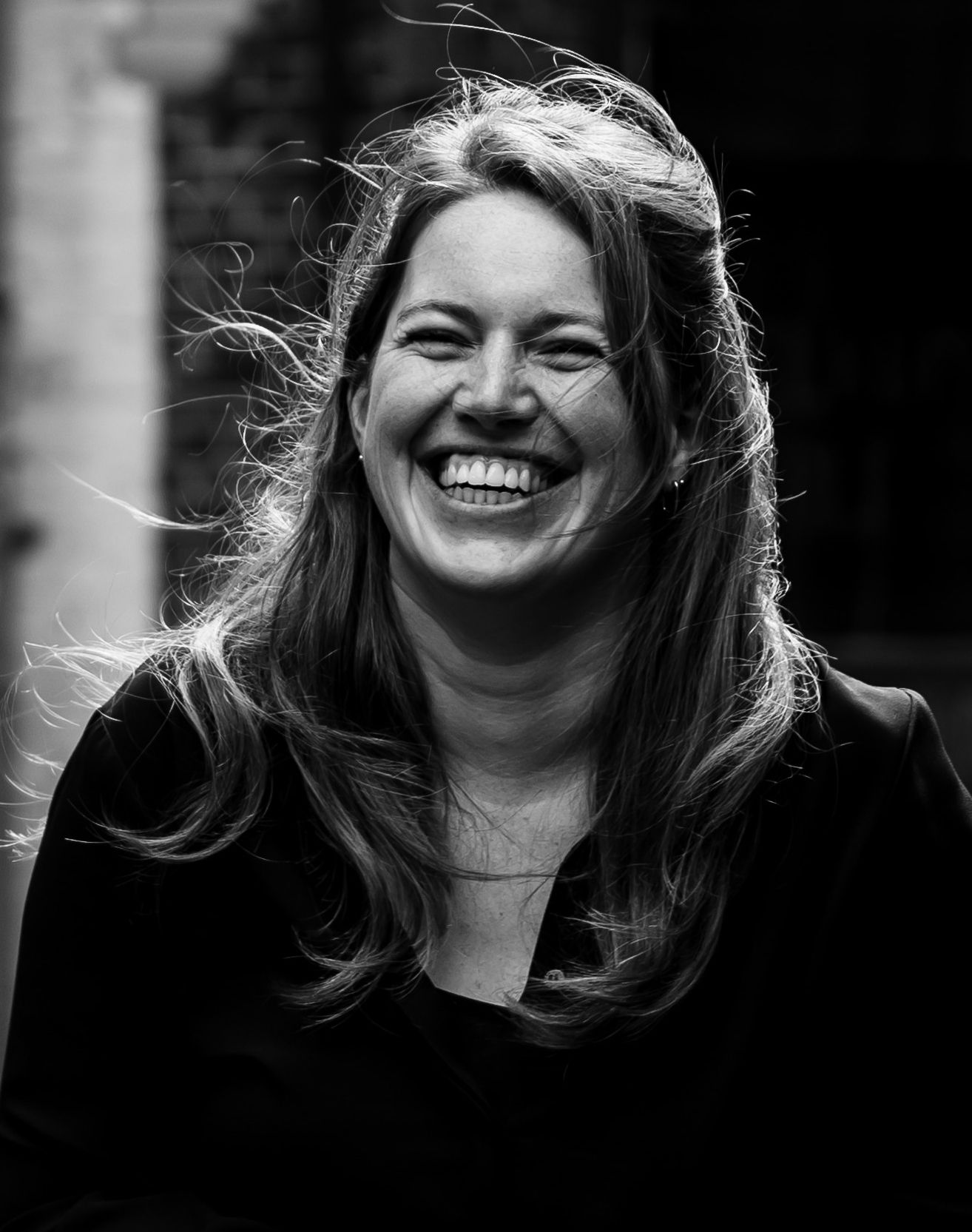 Black and white portrait of a smiling woman with long hair, laughing joyfully outdoors.