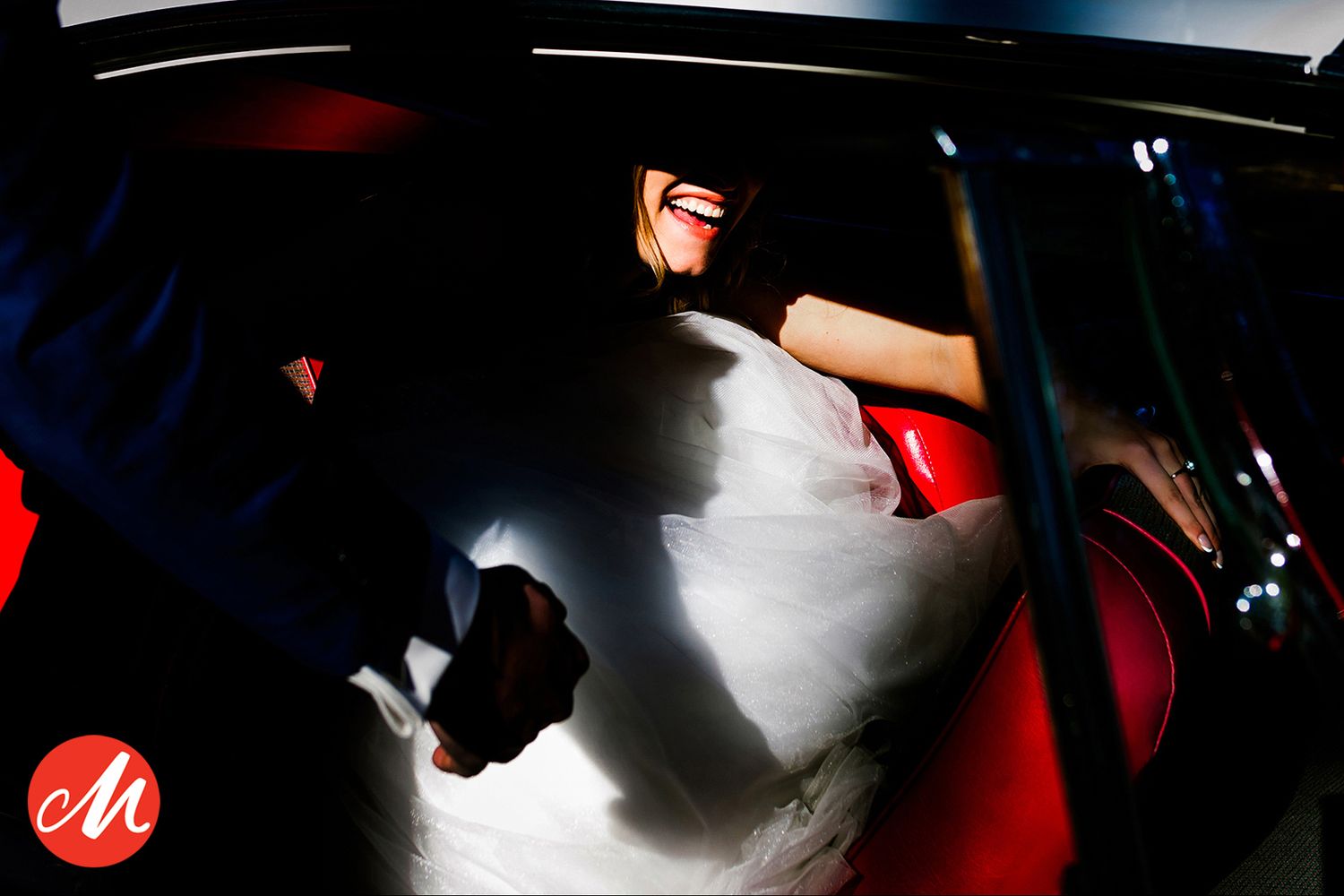 A silhouetted figure in a car with red interior illuminated by dramatic lighting through the window.