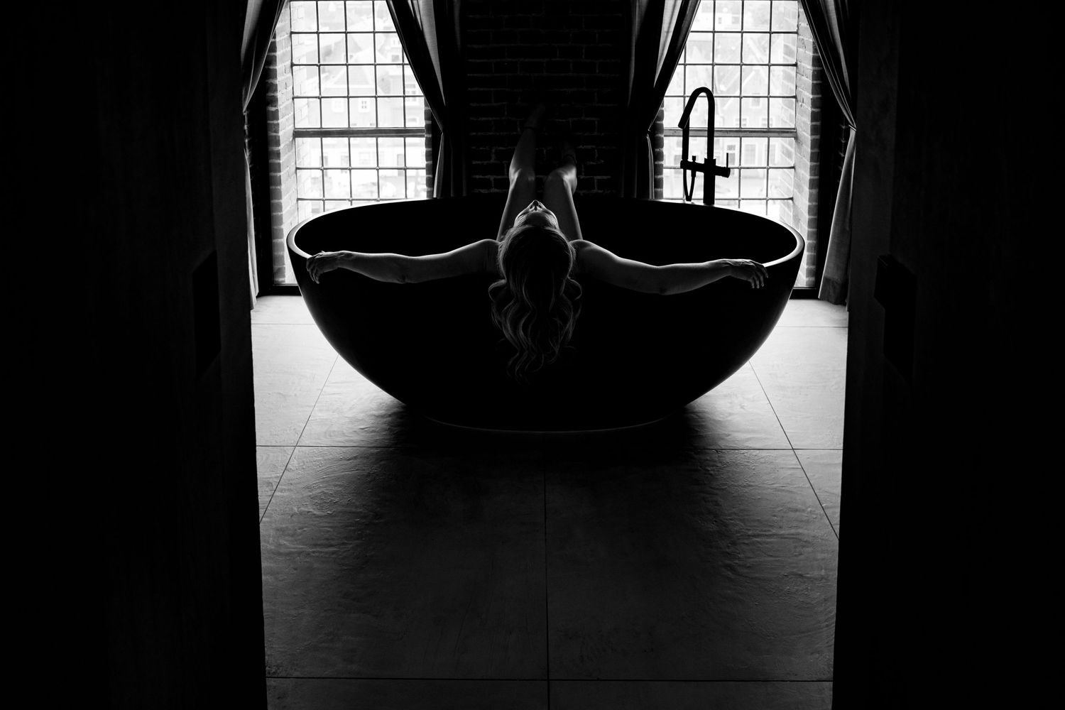Dramatic silhouette of person in bathtub framed by bright windows.